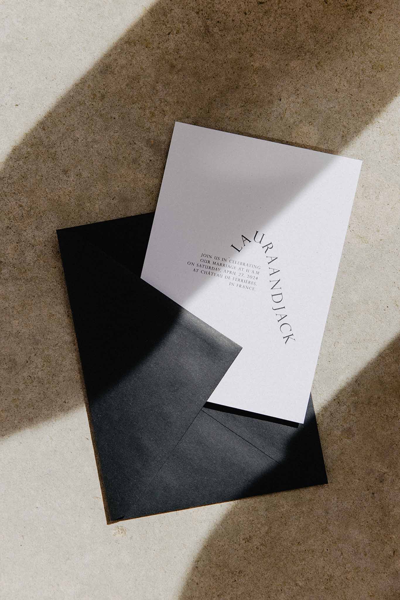 Minimalist wedding invitation with black serif typography and black envelope on concrete surface in natural light