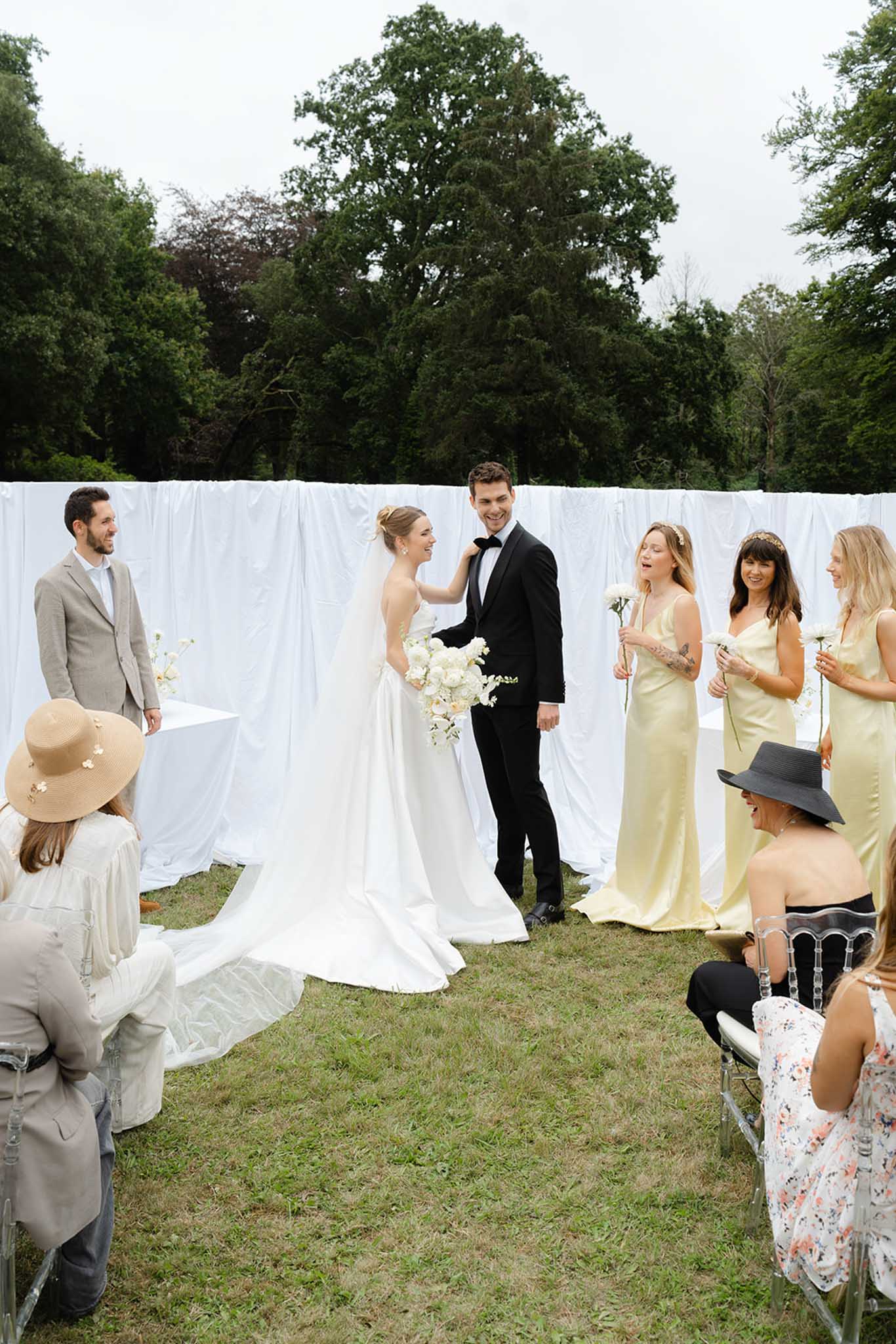 Outdoor garden ceremony with bride, groom, bridesmaids in yellow dresses and guests on white chairs
