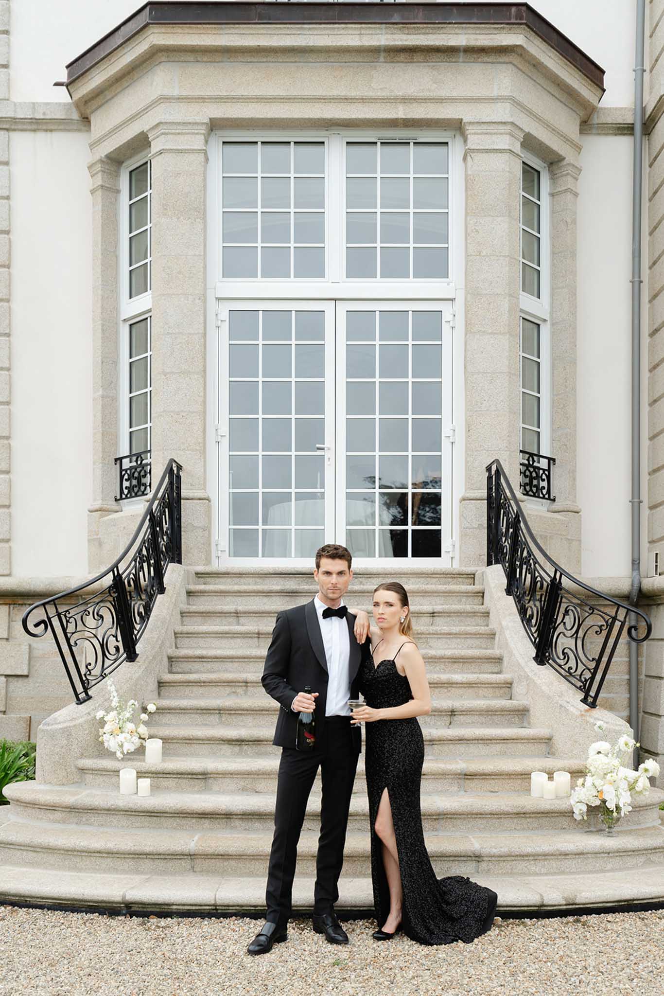 Couple on grand stone steps beside white hydrangea planters and pillar candles at classical cream stone façade