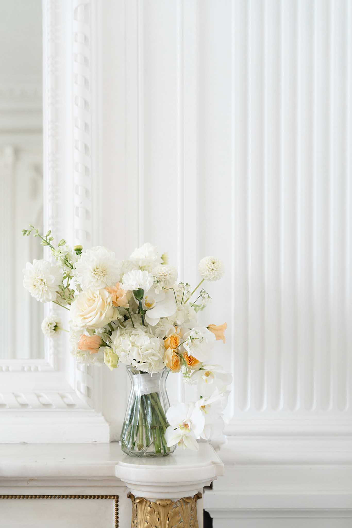 Floral arrangement of cream dahlias, white orchids, and peach roses on gilded pedestal