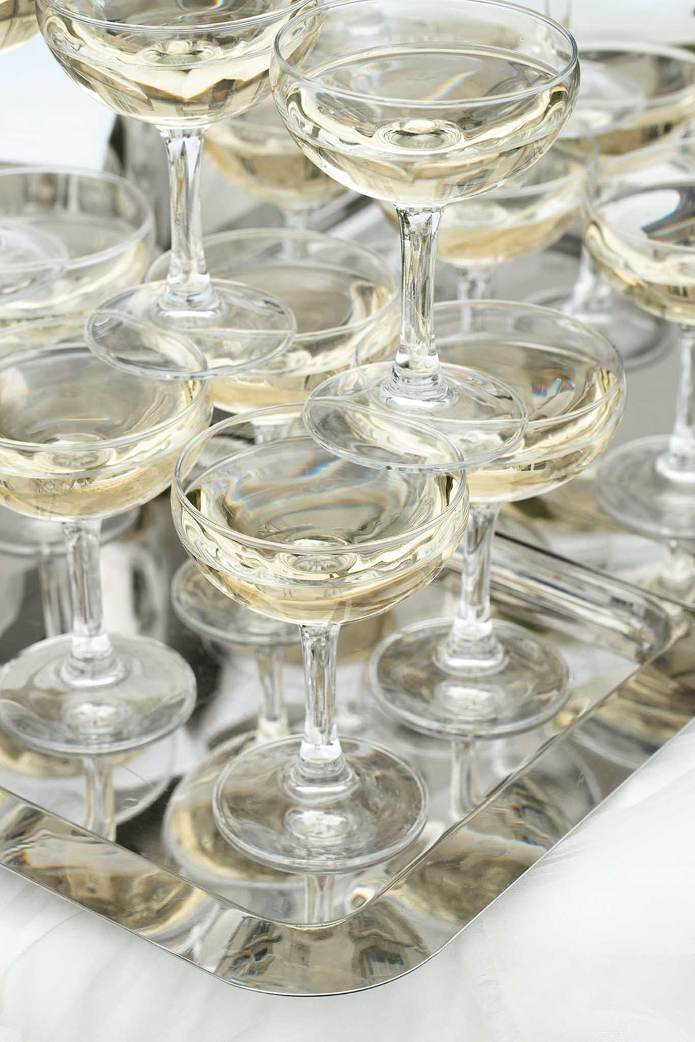 Multiple coupe champagne glasses filled with golden wine arranged on reflective surface with shallow depth of field