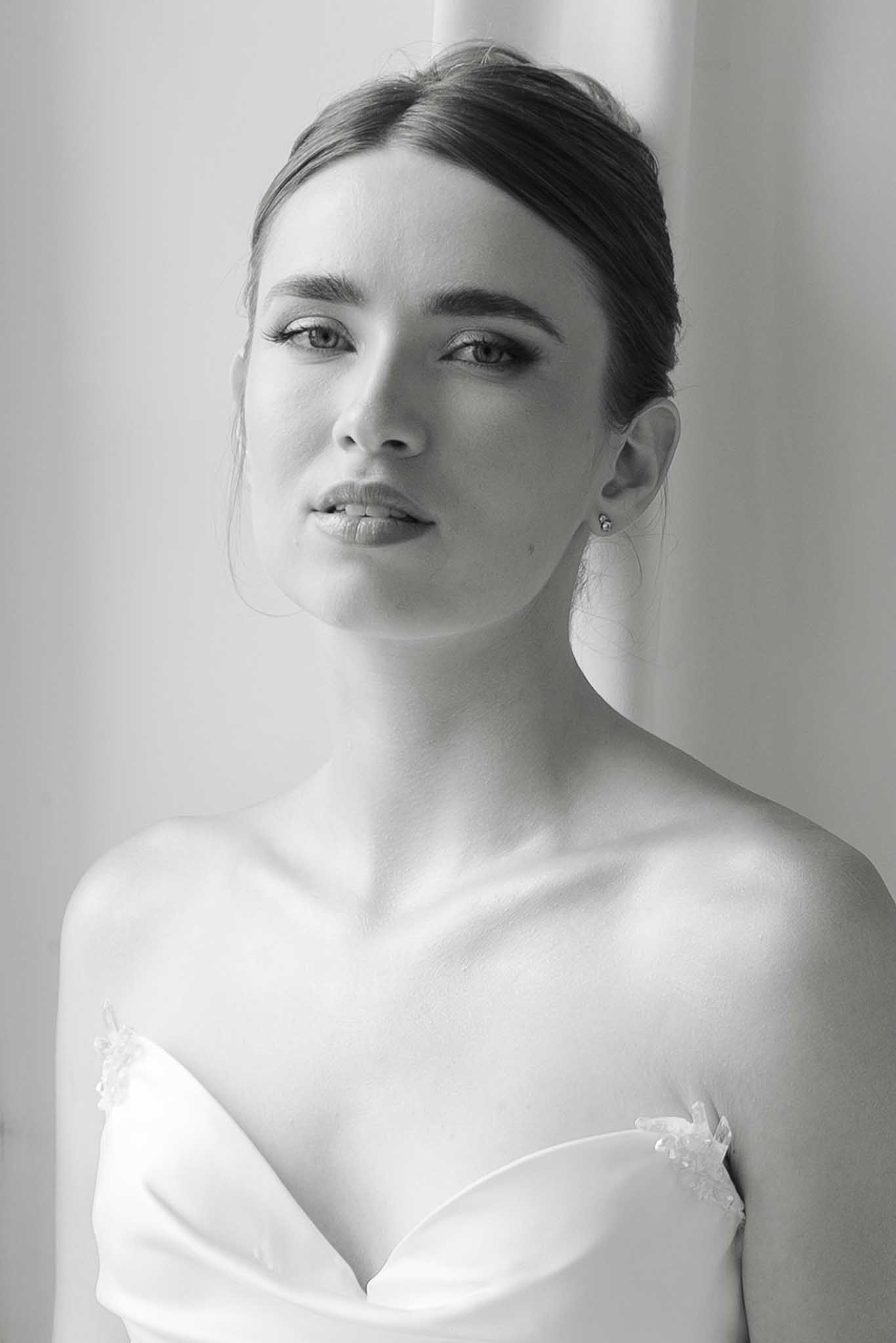 Black and white close-up portrait of bride in a strapless white gown with beaded neckline, dark hair styled to one side.