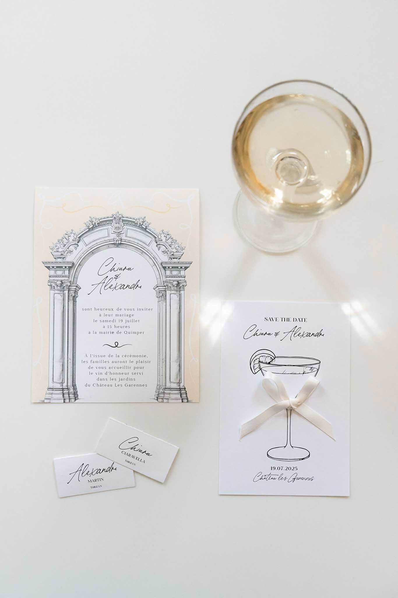 Flat lay of wedding stationery with architectural illustration, save-the-date card, and glass of golden wine