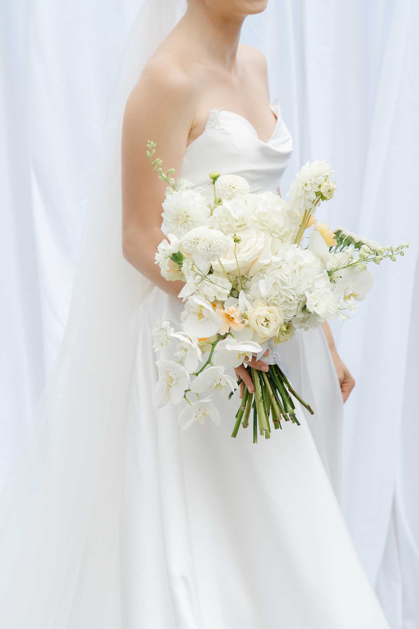 Close-up of bride holding white bouquet of garden roses, dahlias, and ranunculus
