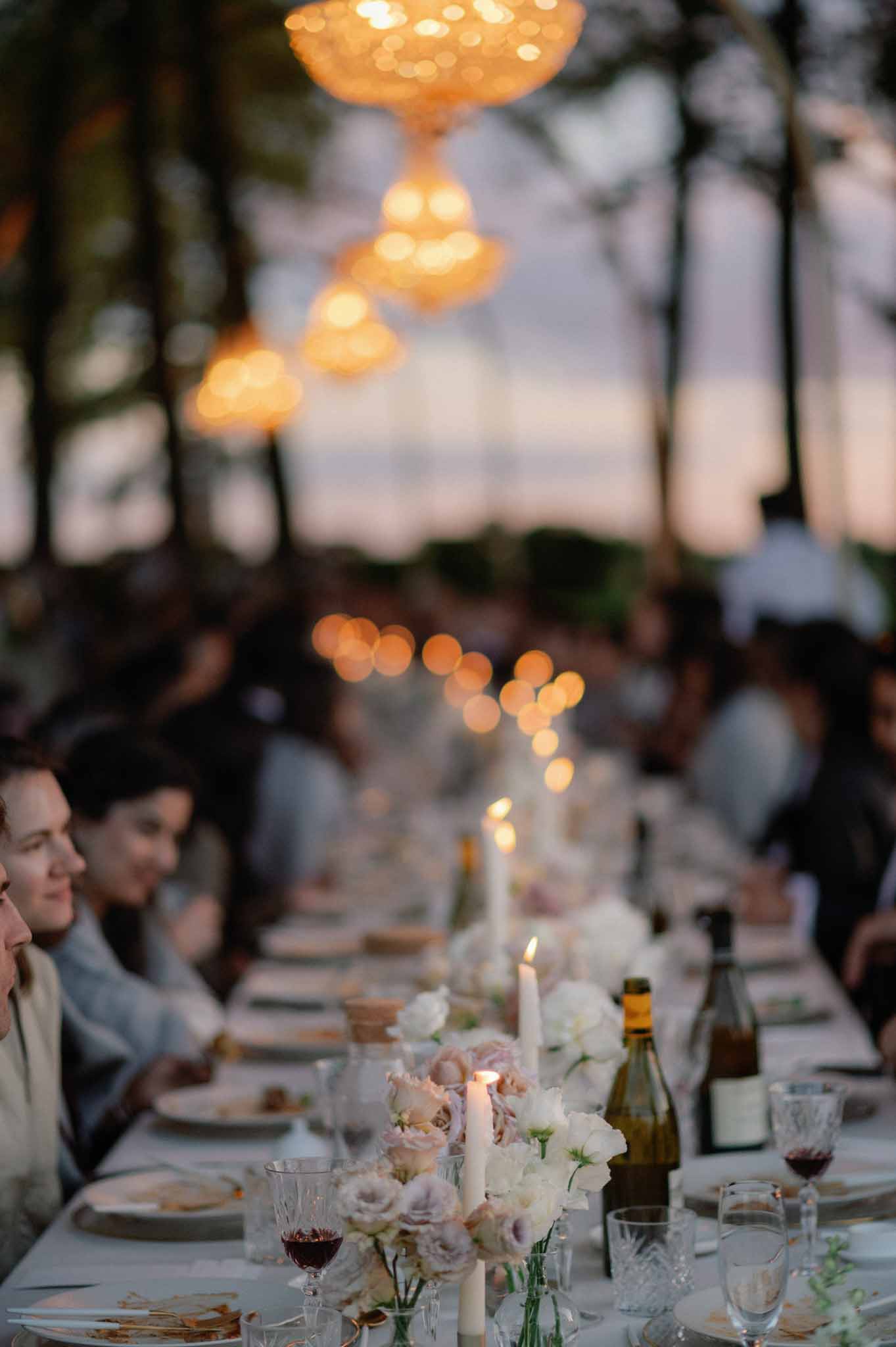 Outdoor reception table detail at golden hour with white carnation centerpieces and amber hanging lanterns