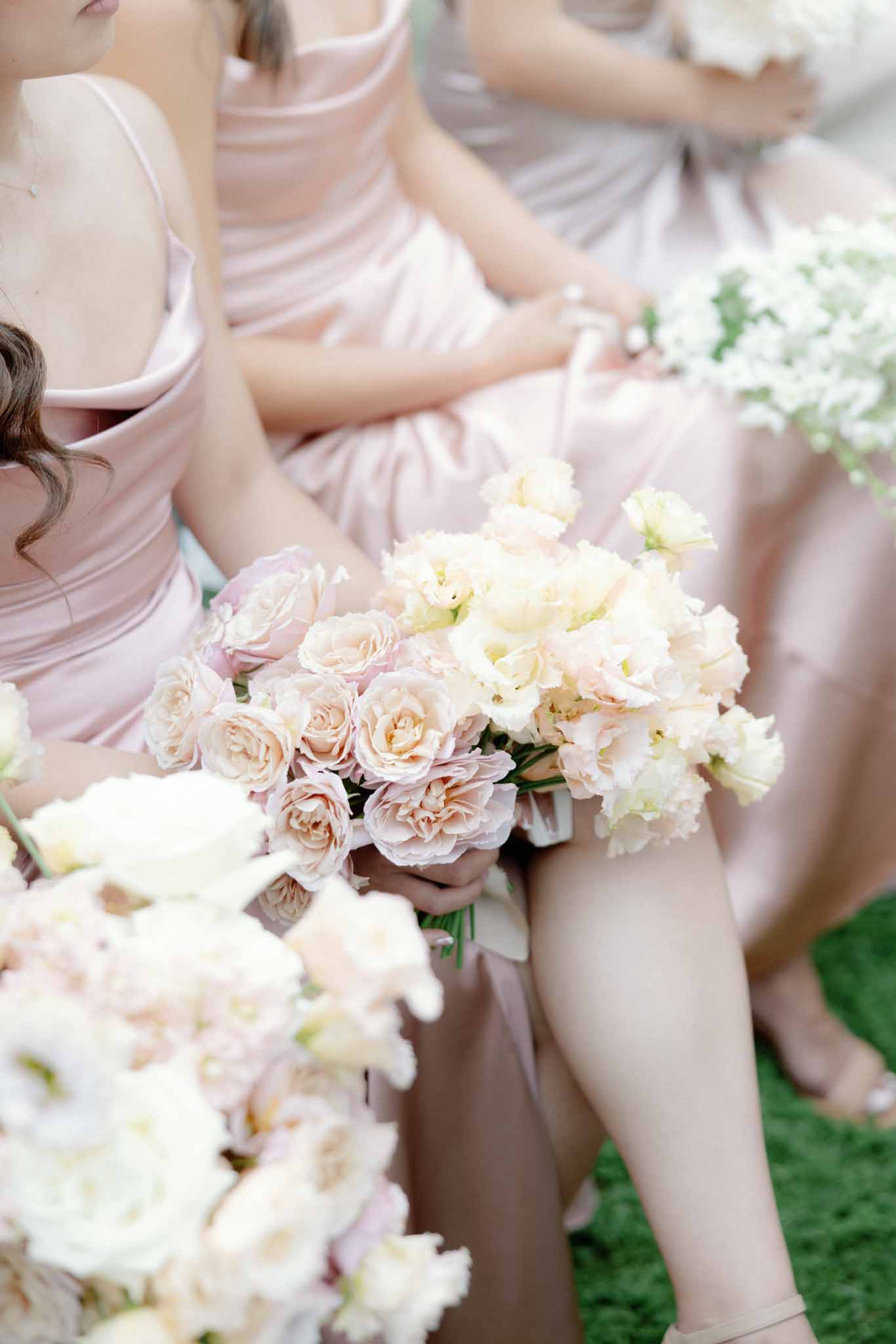 Close-up of bridesmaids in dusty rose dresses holding coordinated blush and ivory rose bouquets