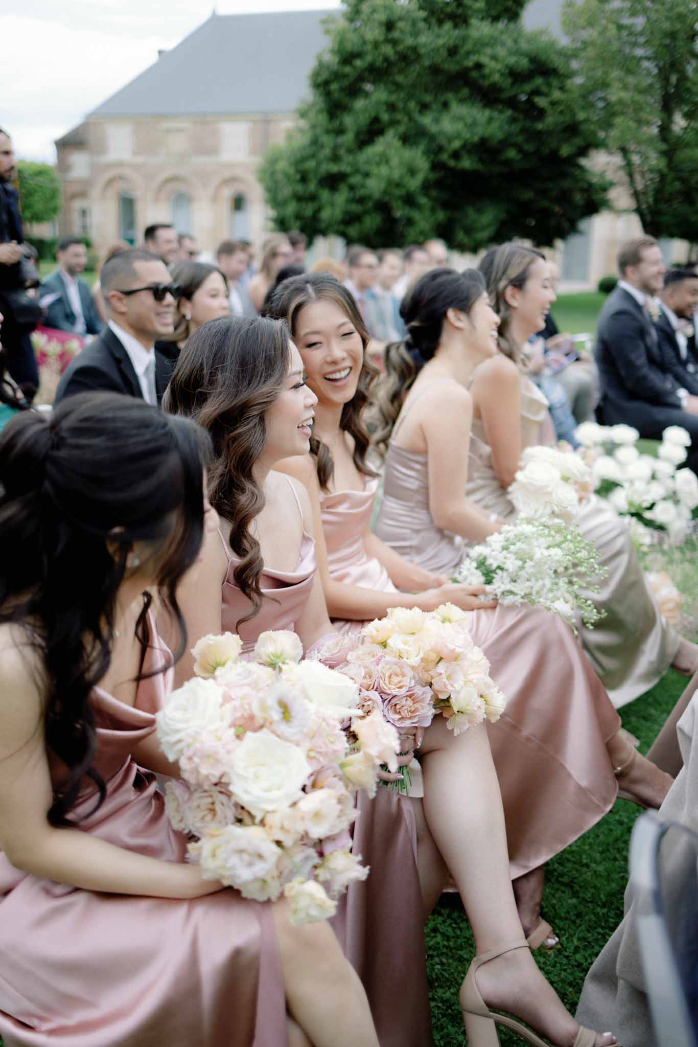 Five bridesmaids in dusty rose gowns holding ivory peony bouquets during outdoor ceremony at classical stone estate