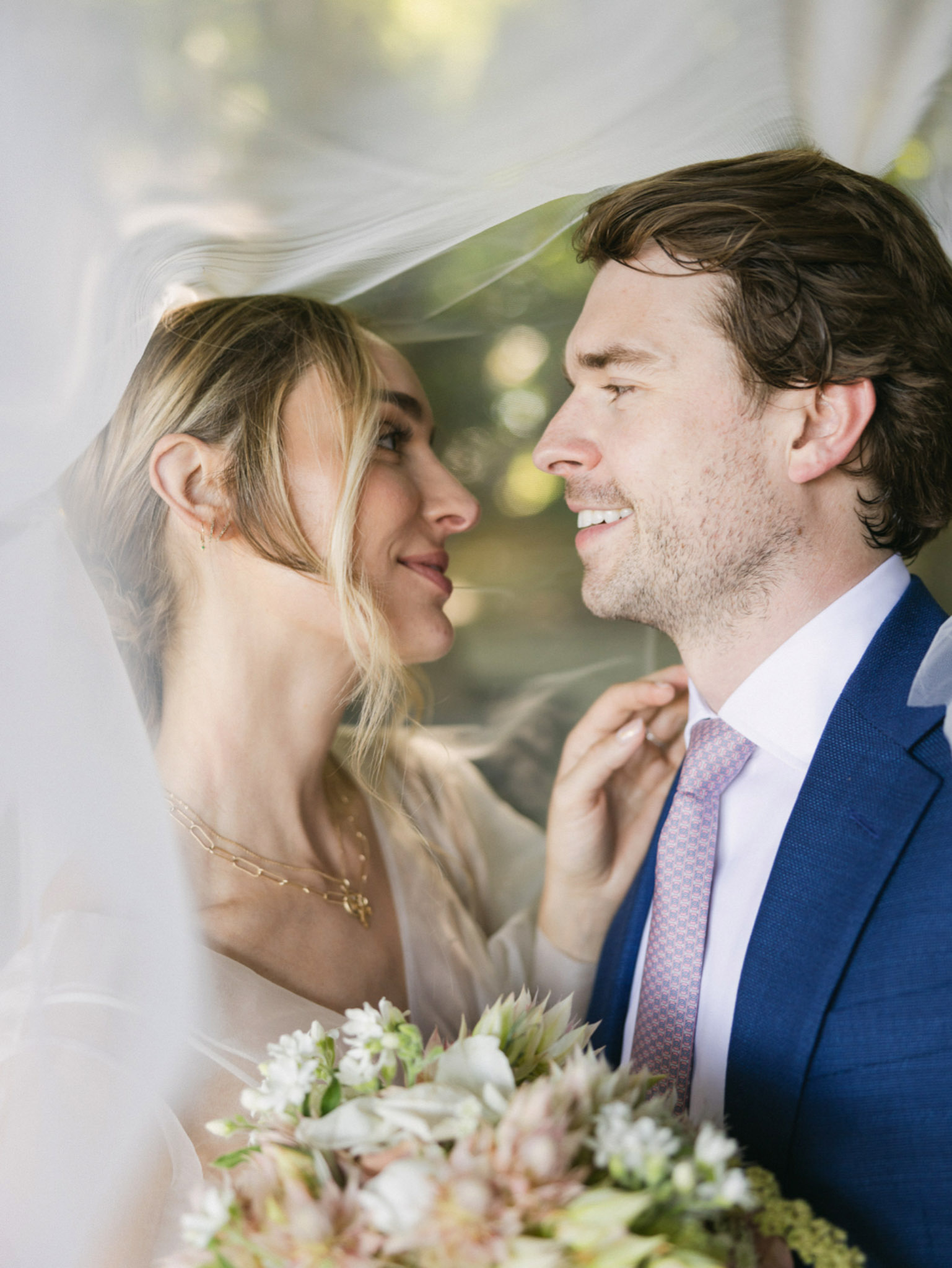 Close-up portrait of bride and groom in profile with white bouquet and warm bokeh background light