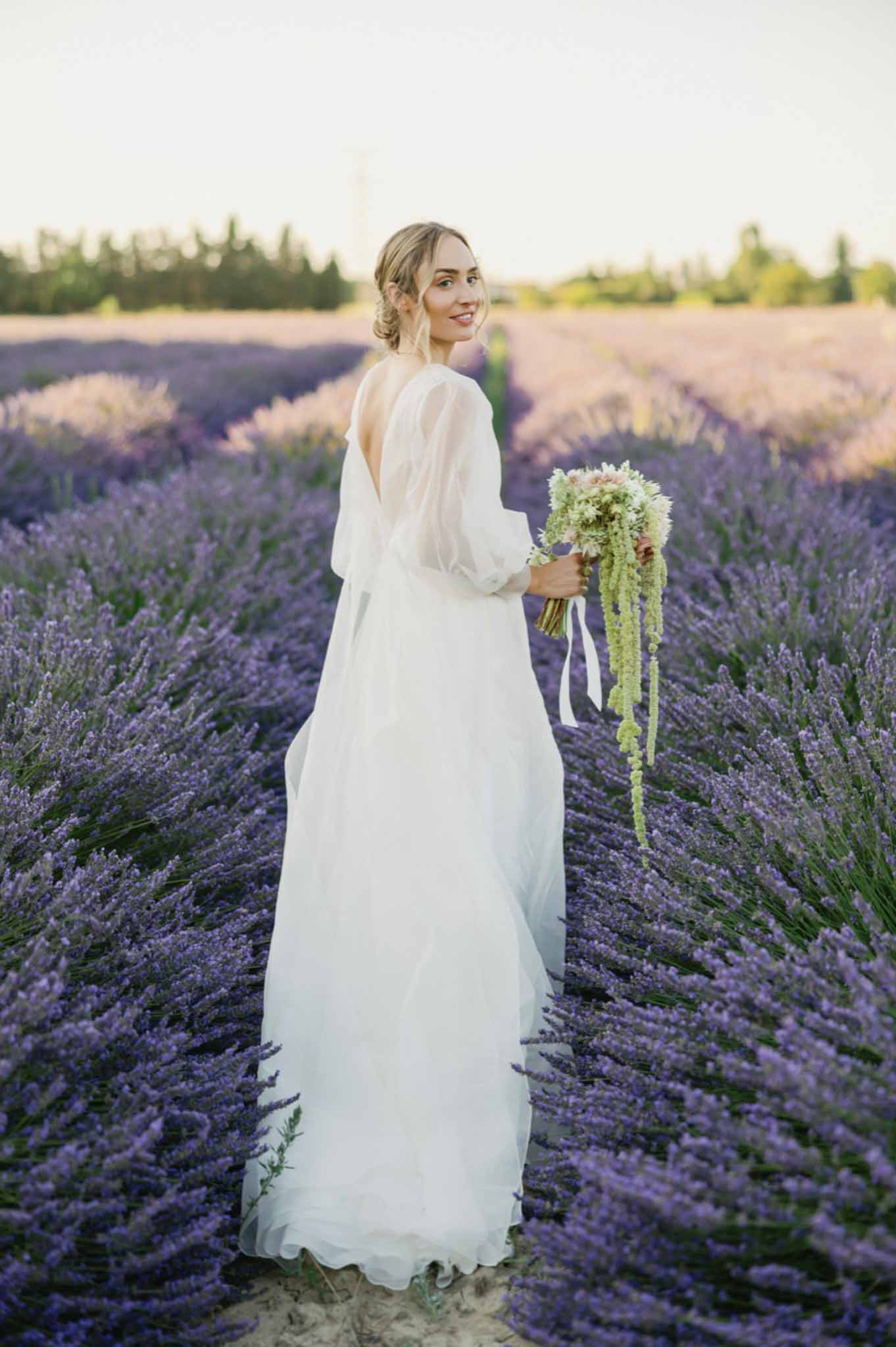 Bride in ivory chiffon gown with cascading green amaranthus bouquet stands in lavender field at golden hour