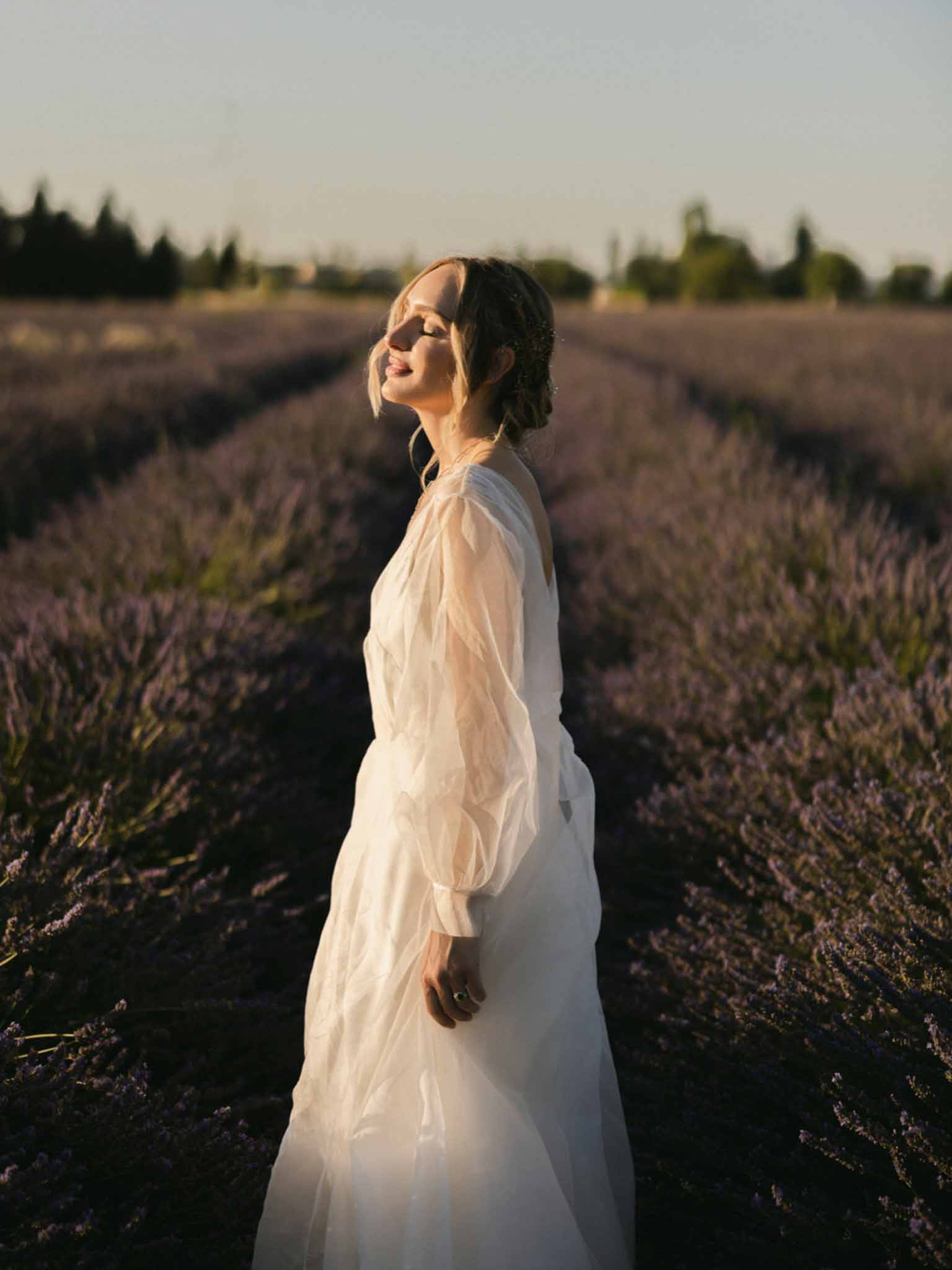 Bride in ivory long-sleeve dress posing in lavender field at golden hour