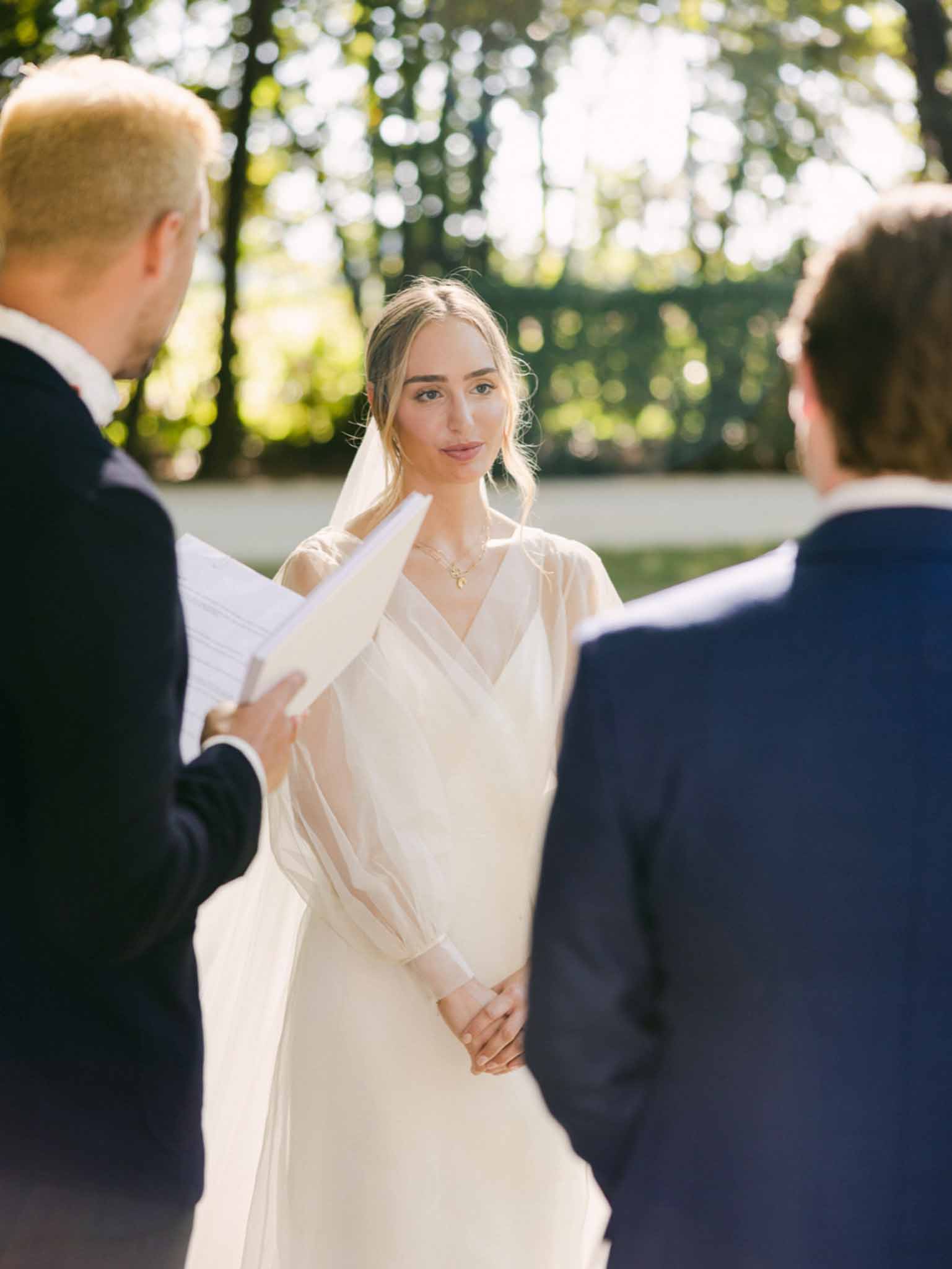 Bride and groom exchanging vows in an outdoor garden ceremony framed by tall hedges and dappled light