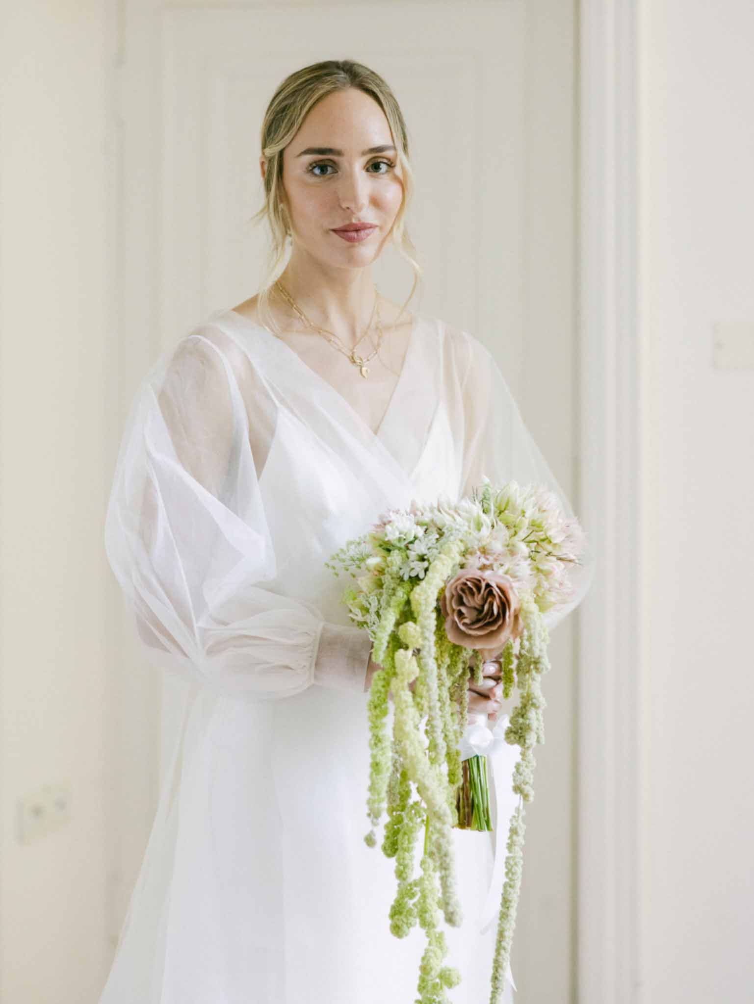 Bride in ivory wrap dress holding cascading bouquet with dusty mauve rose, pink spray roses, and trailing amaranthus