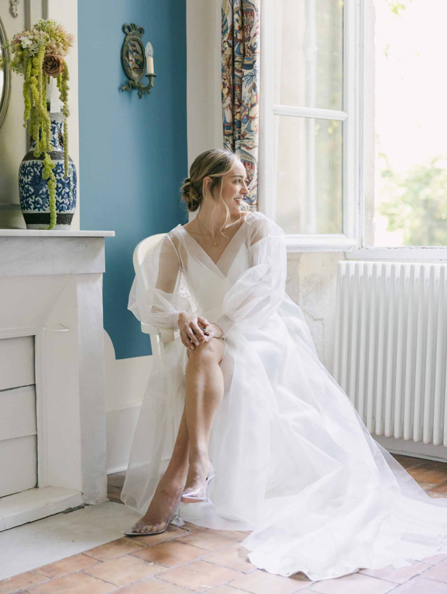 Bride seated in elegant room with teal walls wearing ivory chiffon wrap gown before ceremony