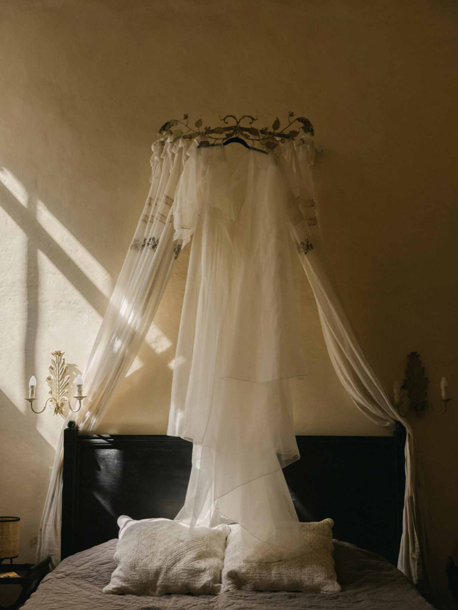 Ornate four-poster bed with black frame and sheer ivory tulle canopy draping in bridal preparation suite