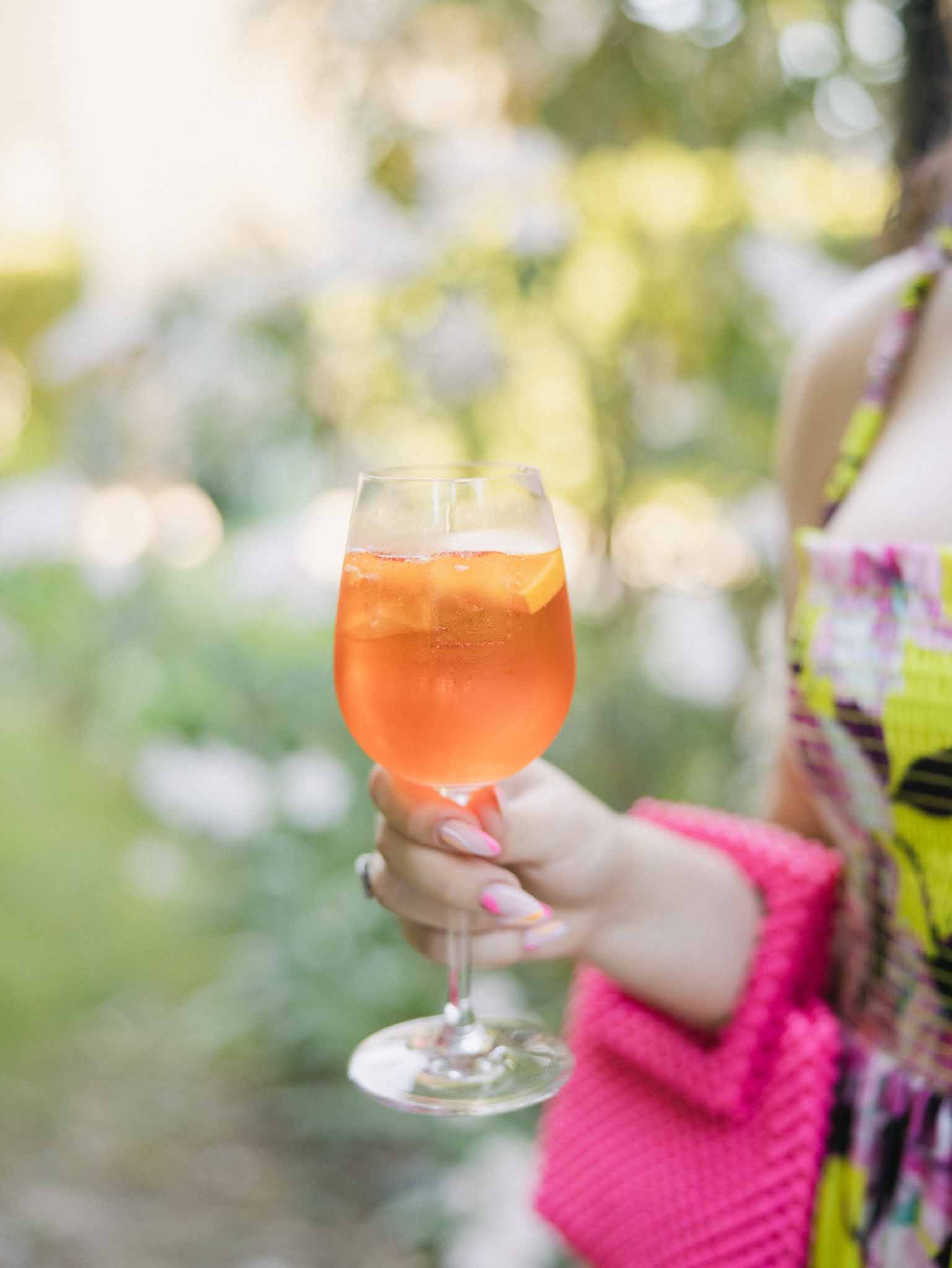 Close-up of guest holding orange spritz cocktail in garden during outdoor cocktail hour