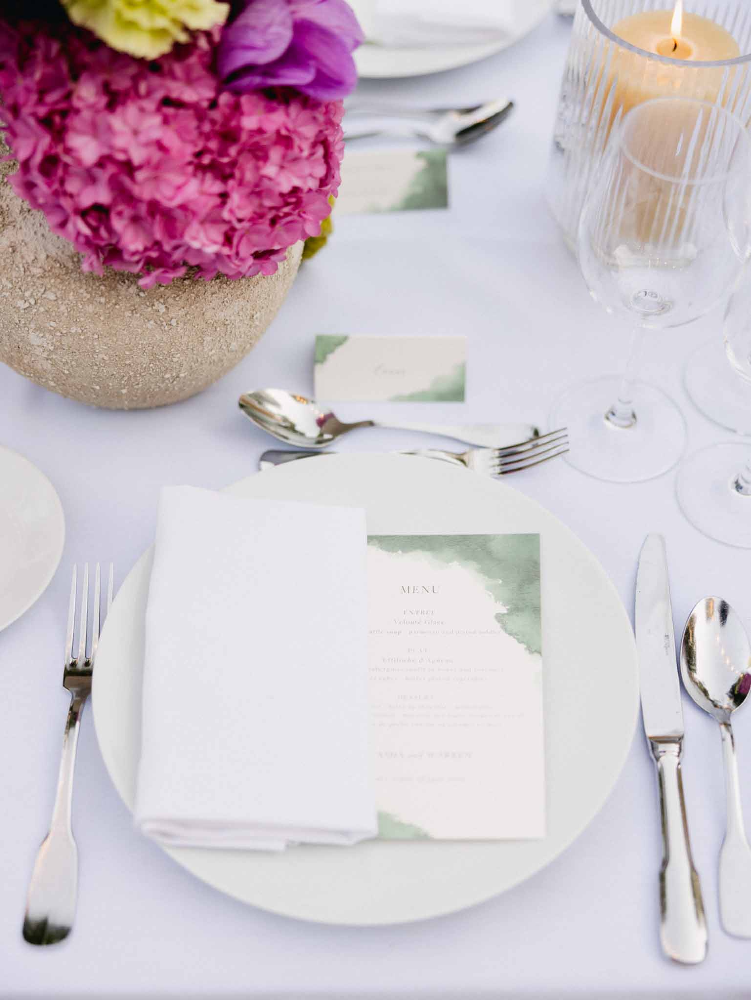 Overhead reception place setting with magenta hydrangea centerpiece in gold vase and pale green menu card