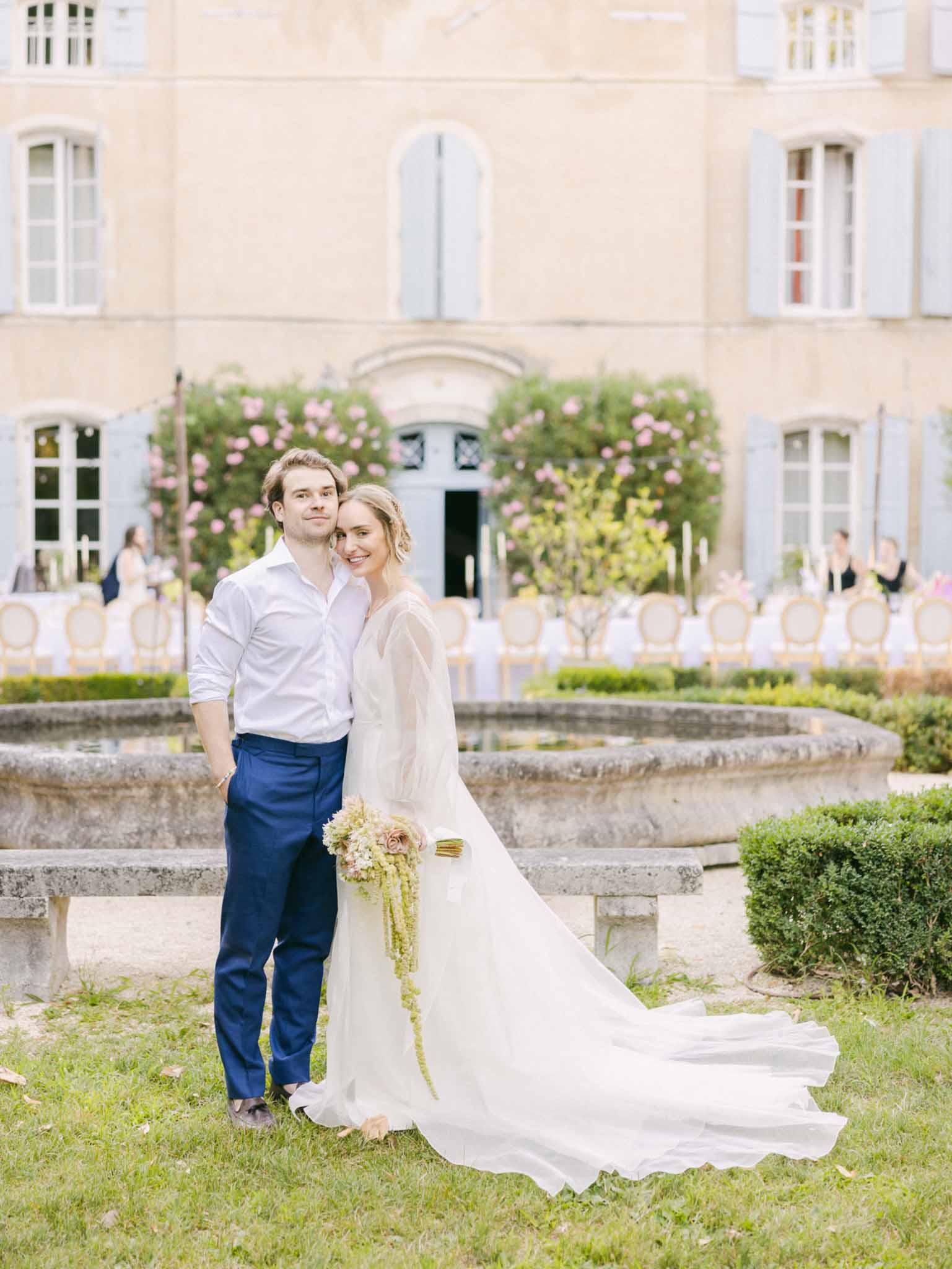 Bride and groom posing in the courtyard of a stone chateau with floral entrance installation and Chiavari chairs