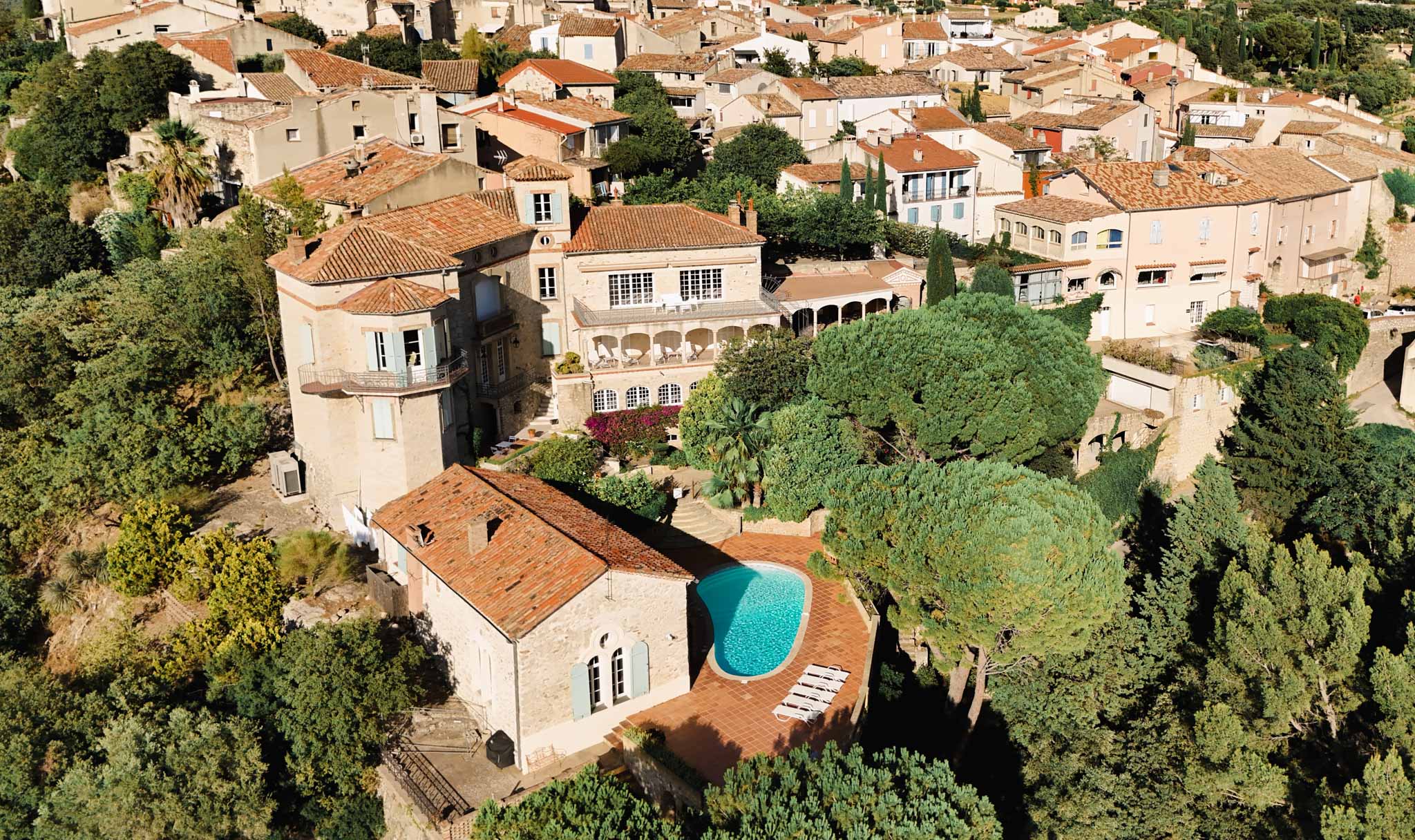 Aerial view of Provencal village estate with terracotta roofs, kidney pool, and colonnade terrace
