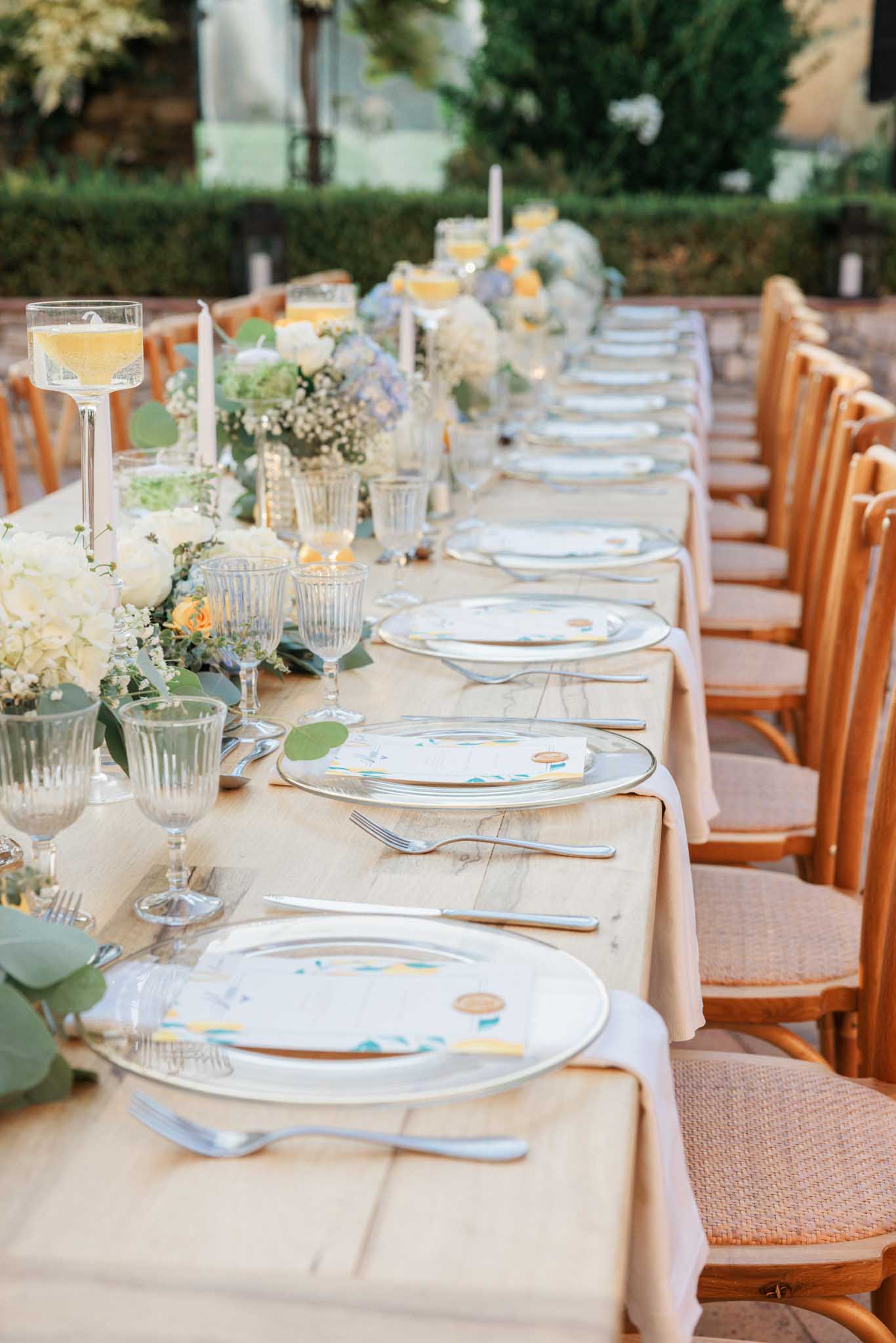Reception table with watercolor-design plates, white hydrangea centerpieces, and wooden orange-upholstered chairs