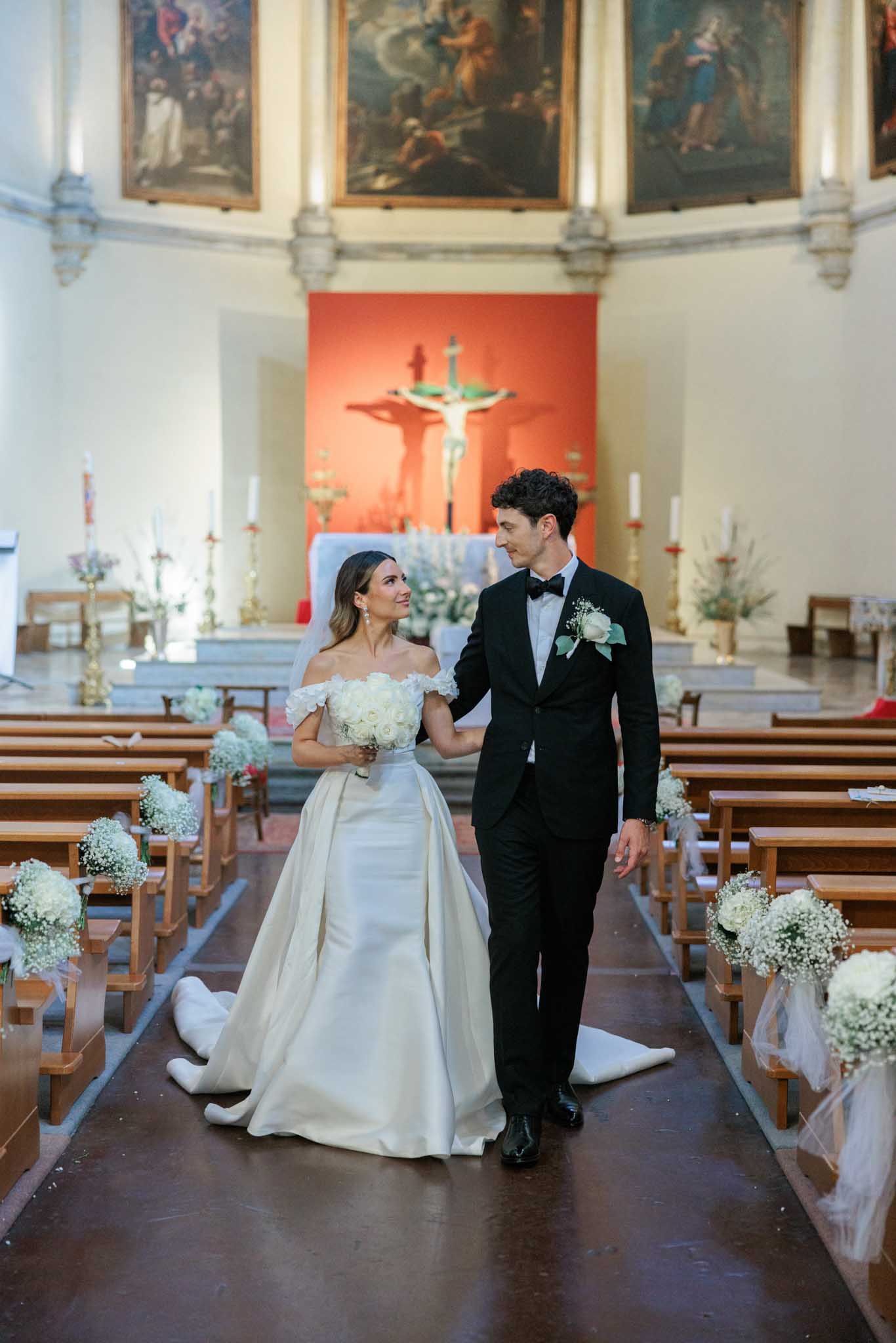 Bride and groom walking down the aisle of a neoclassical chapel decorated with baby's breath pew arrangements