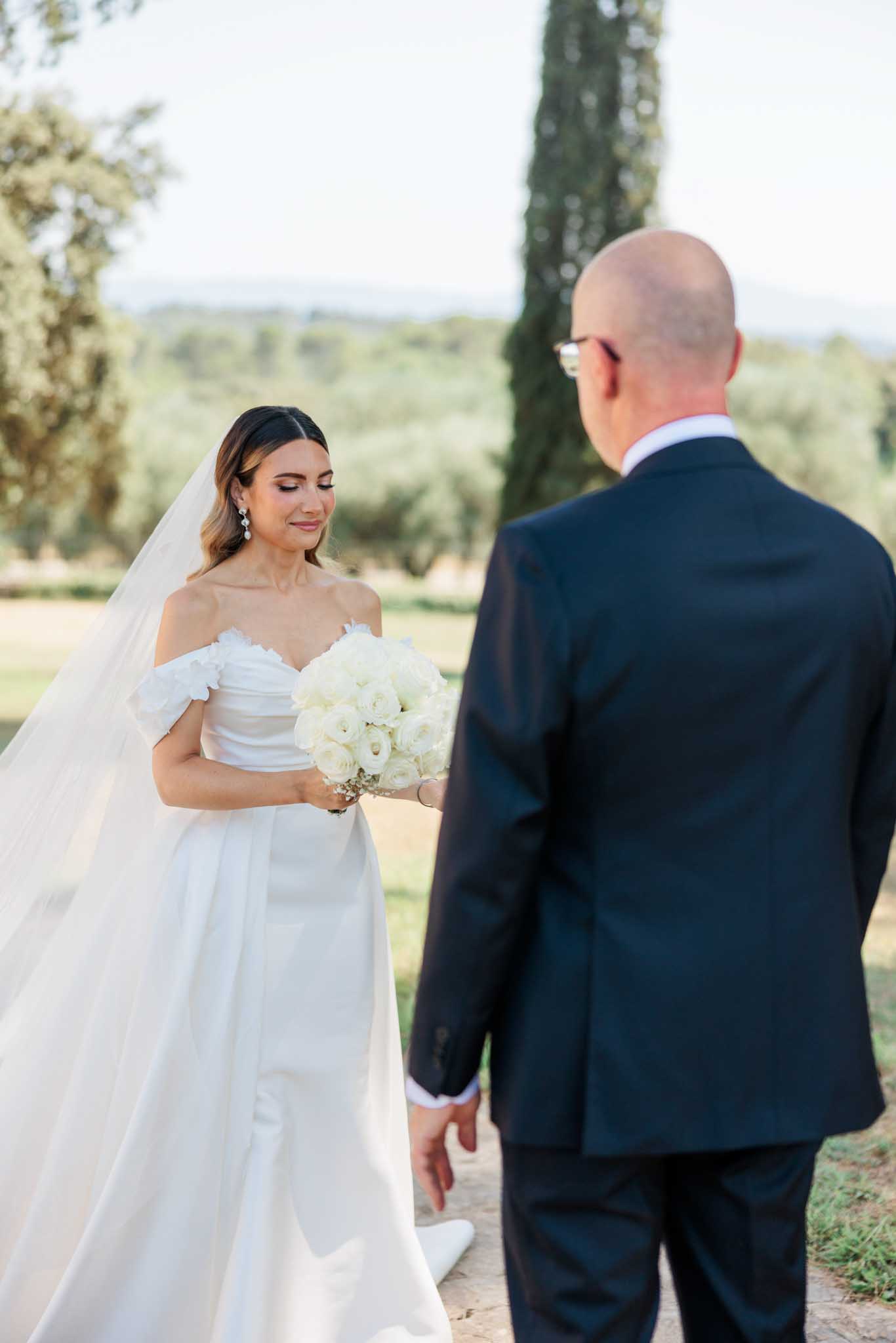 Bride and groom facing each other in outdoor garden with cypress trees during first look