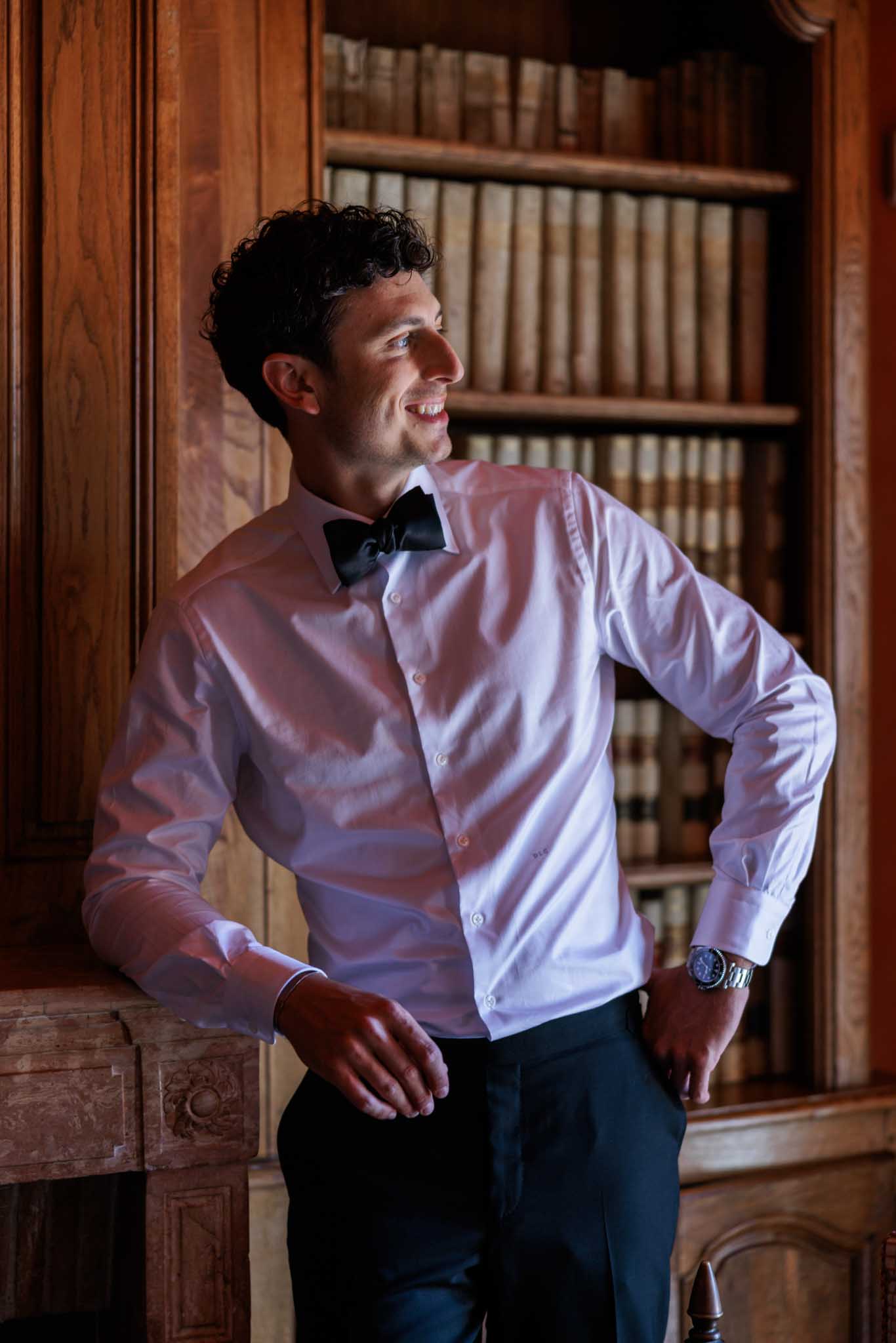 Groom in white shirt and bow tie posed against carved wooden panelling and bookshelves