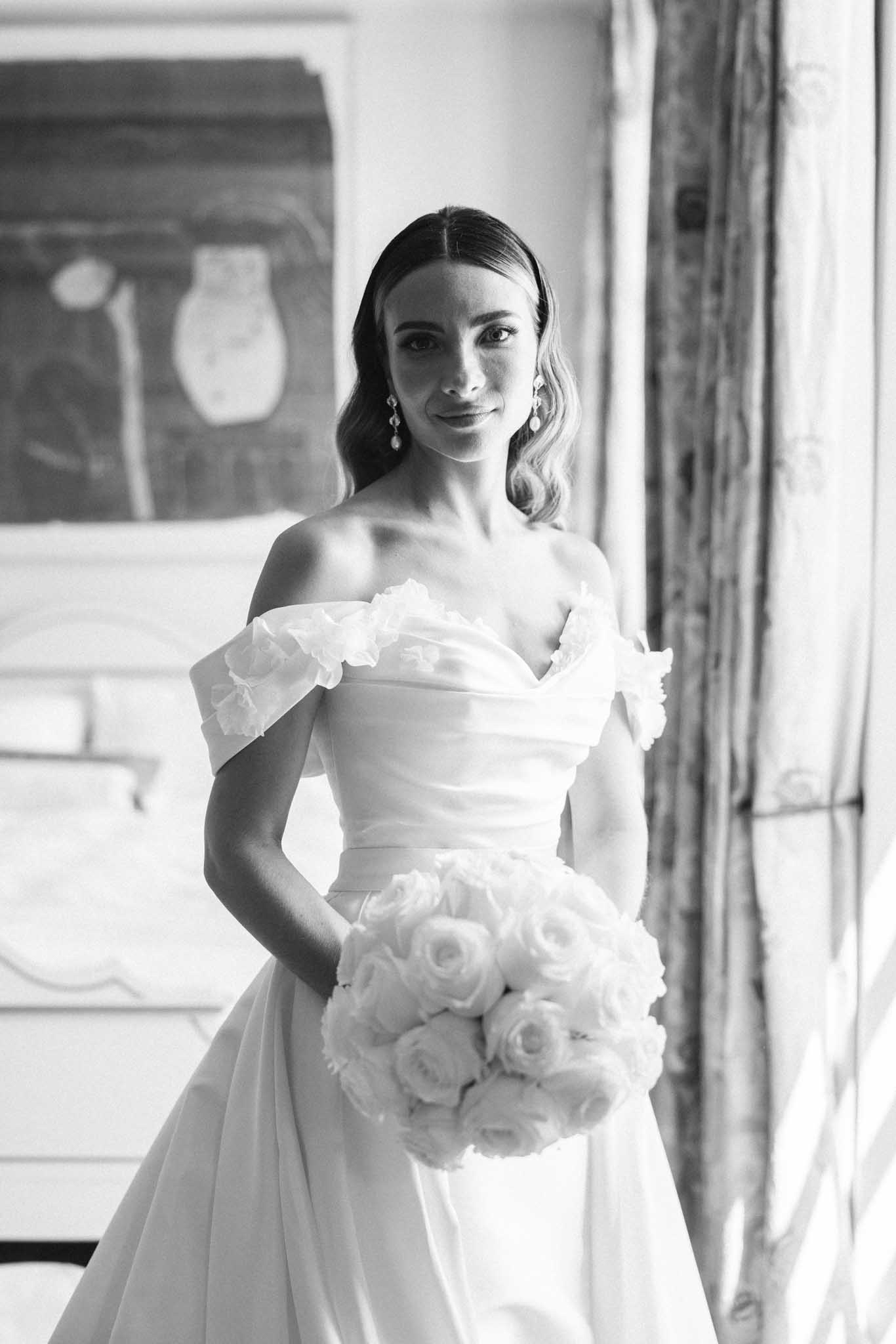 Black and white portrait of bride in strapless gown holding rose bouquet in modern interior