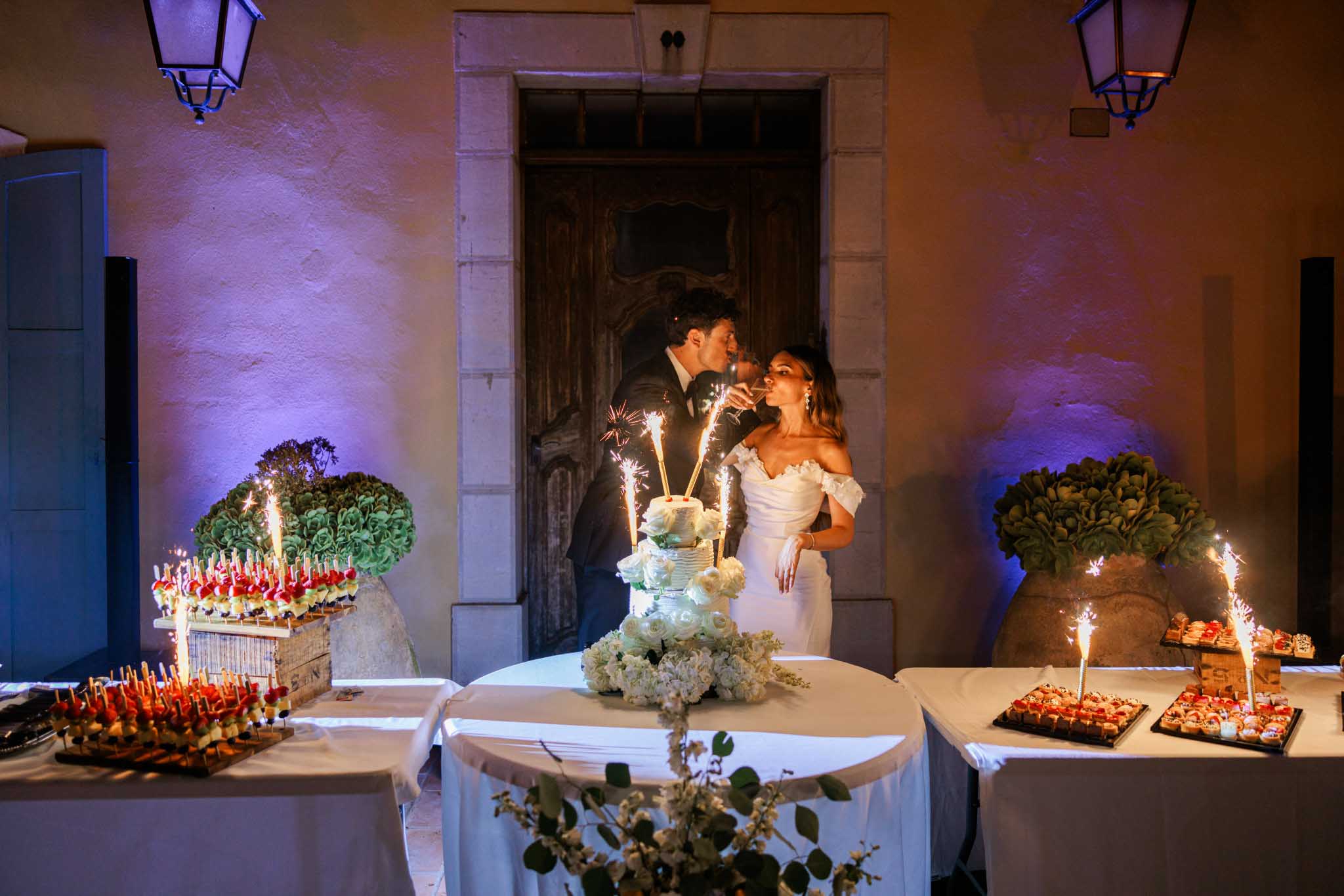 Bride and groom cutting cake in stone courtyard with purple uplighting