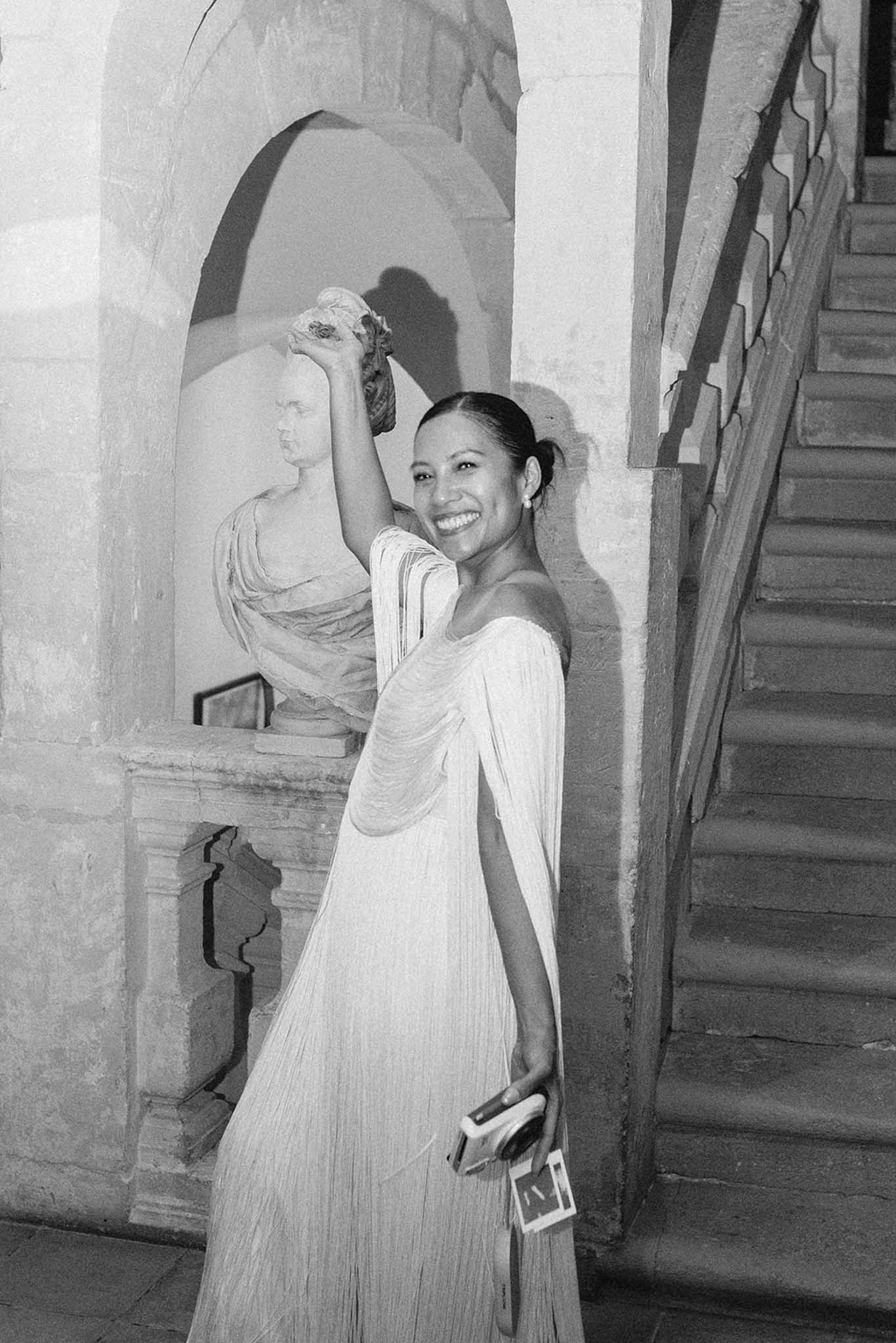 Black-and-white bride in pleated gown beside classical bust in stone passageway