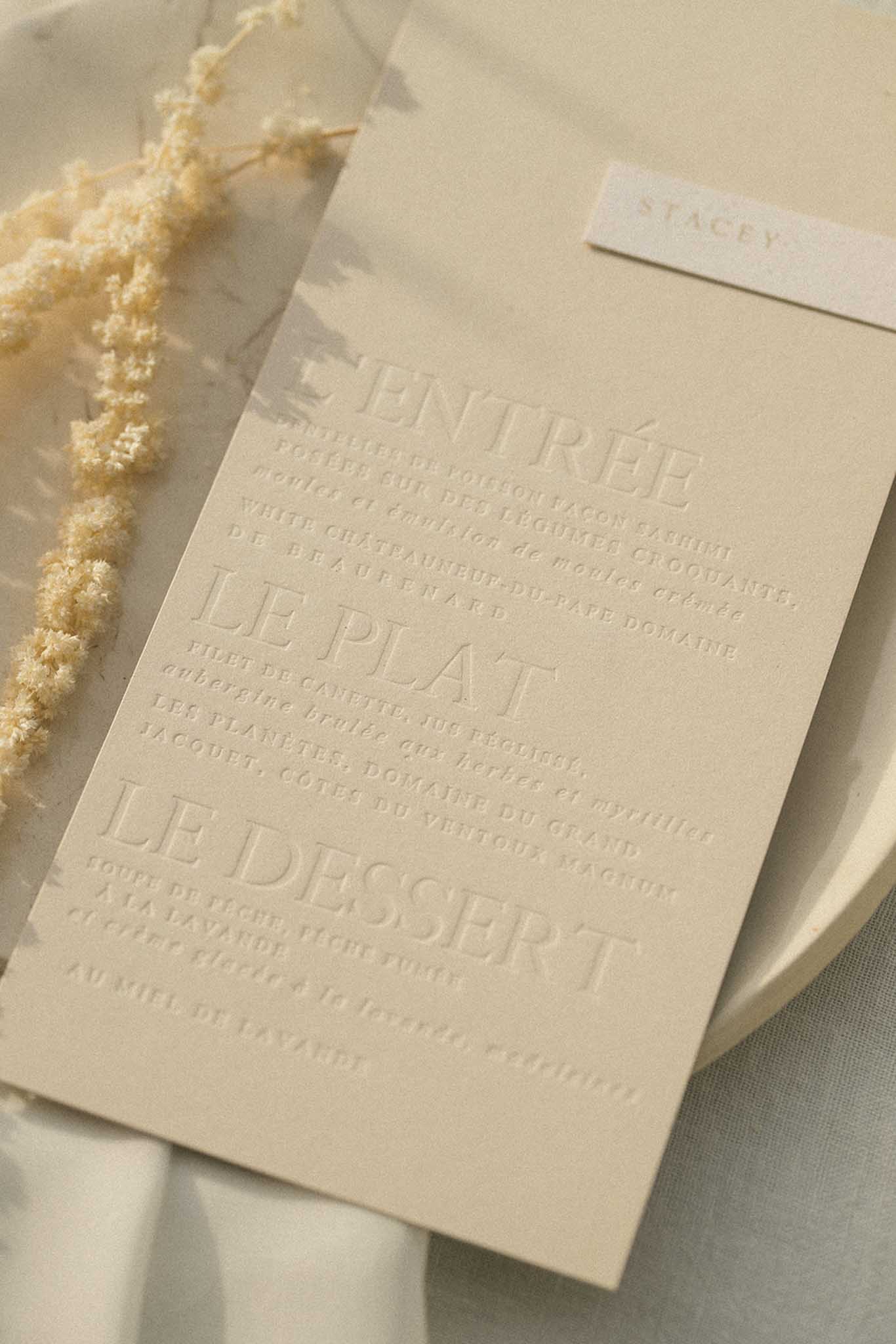 French wedding menu cards on cream cardstock with embossed text and dried pampas grass on white linen