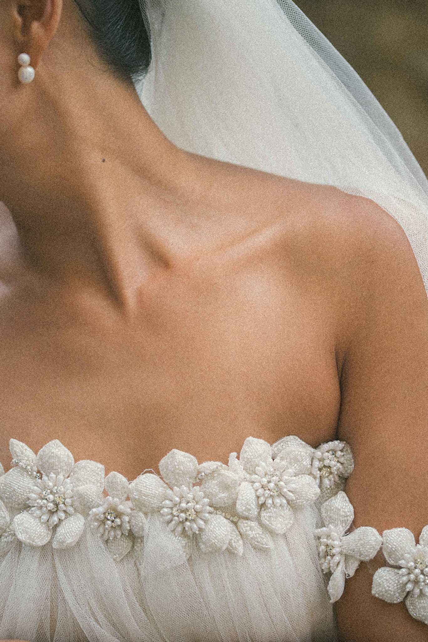 Close-up of bridal bodice with beaded floral appliques, pearl earrings, and draped veil