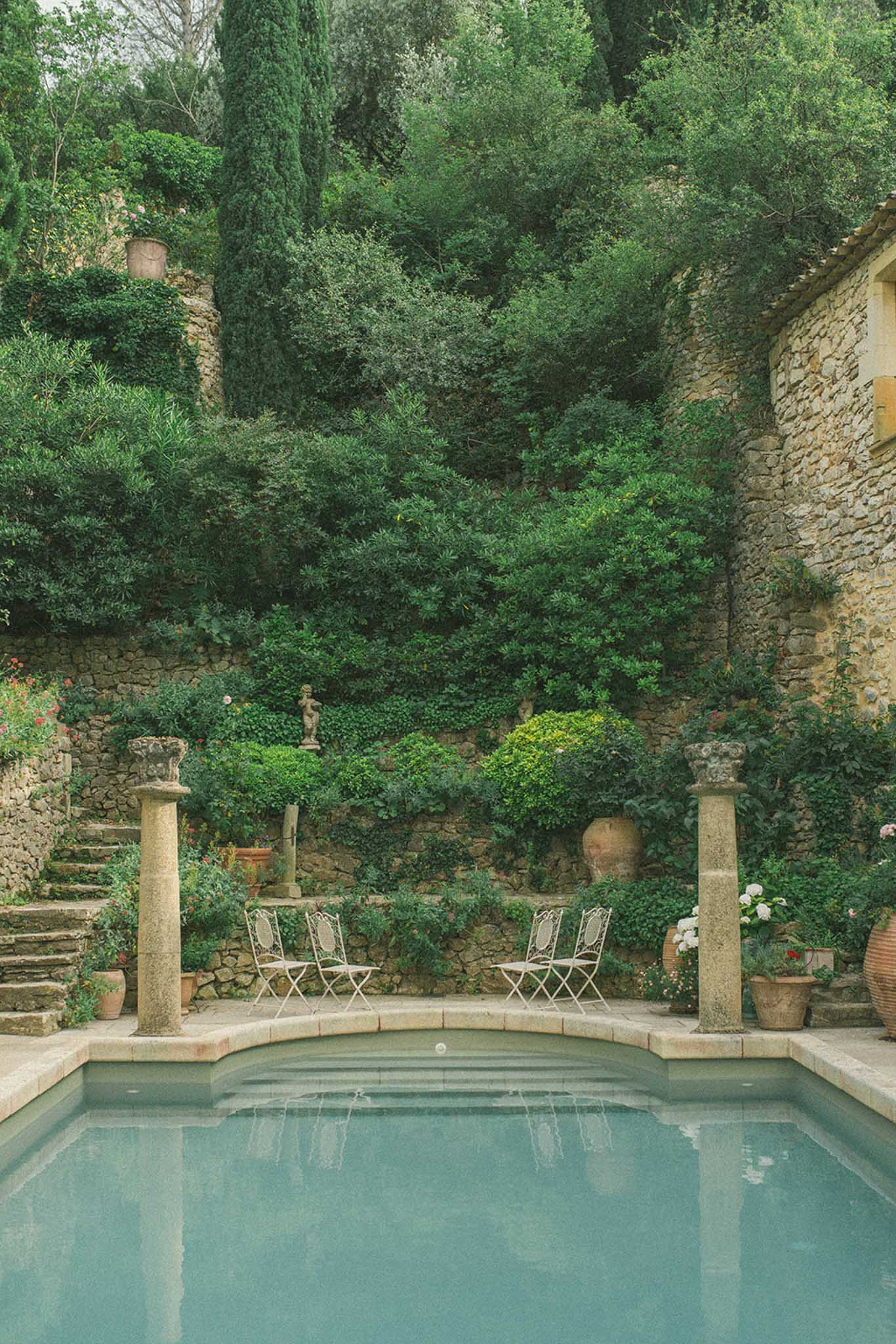Stone-walled courtyard with turquoise pool, ivy-covered walls, cypress trees, and director chairs at historic venue