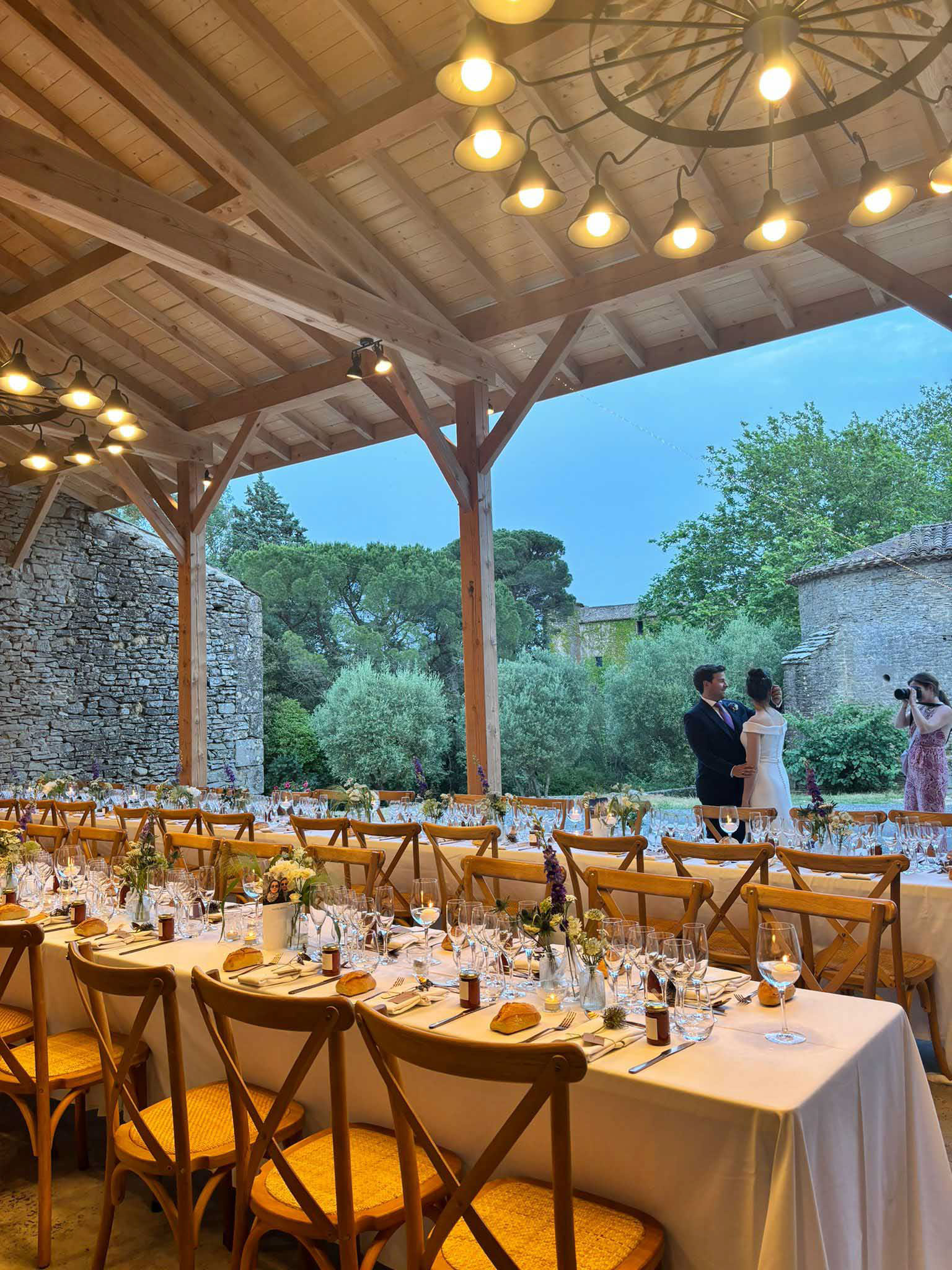 Pergola reception with Edison pendants, yellow-green florals, and cross-back chairs at Provencal mas