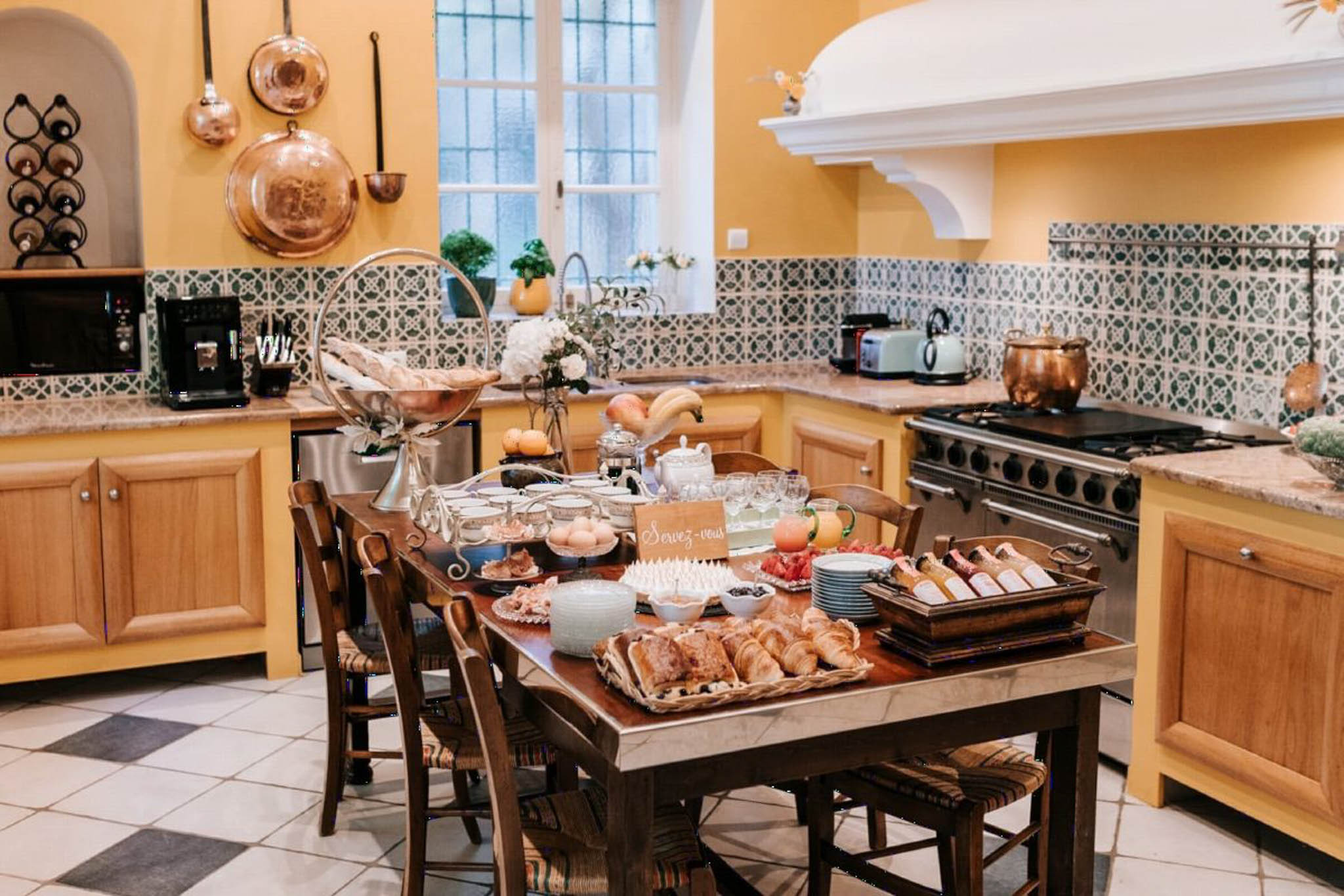 French country kitchen with copper pans, checkered floor, and breakfast buffet spread