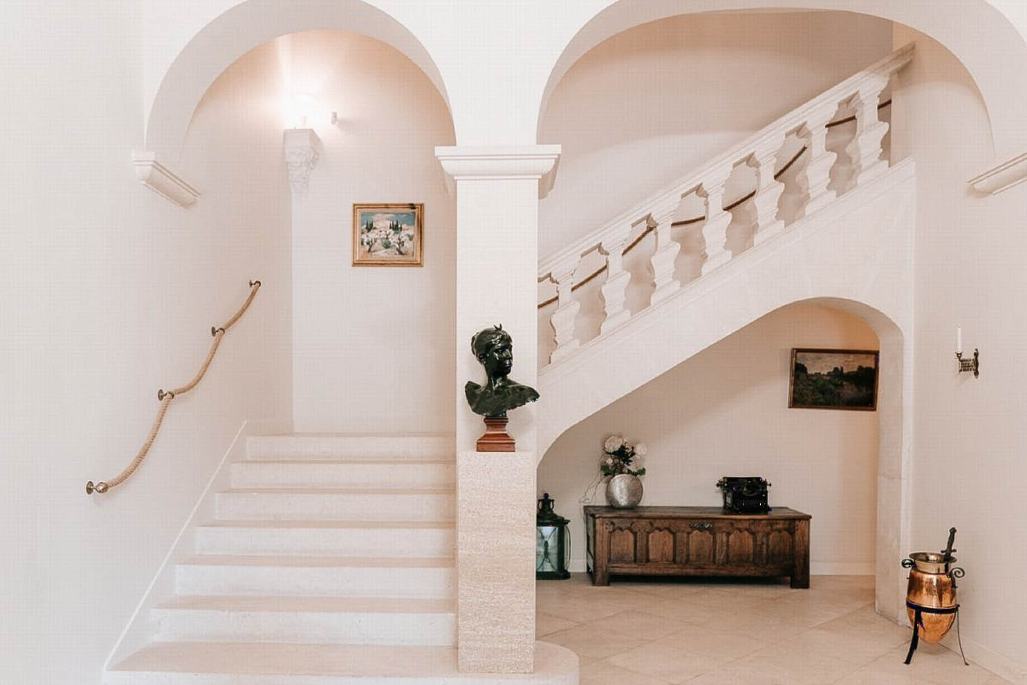 Chateau entrance hall with twin sweeping staircases, bronze bust sculpture, and antique console table