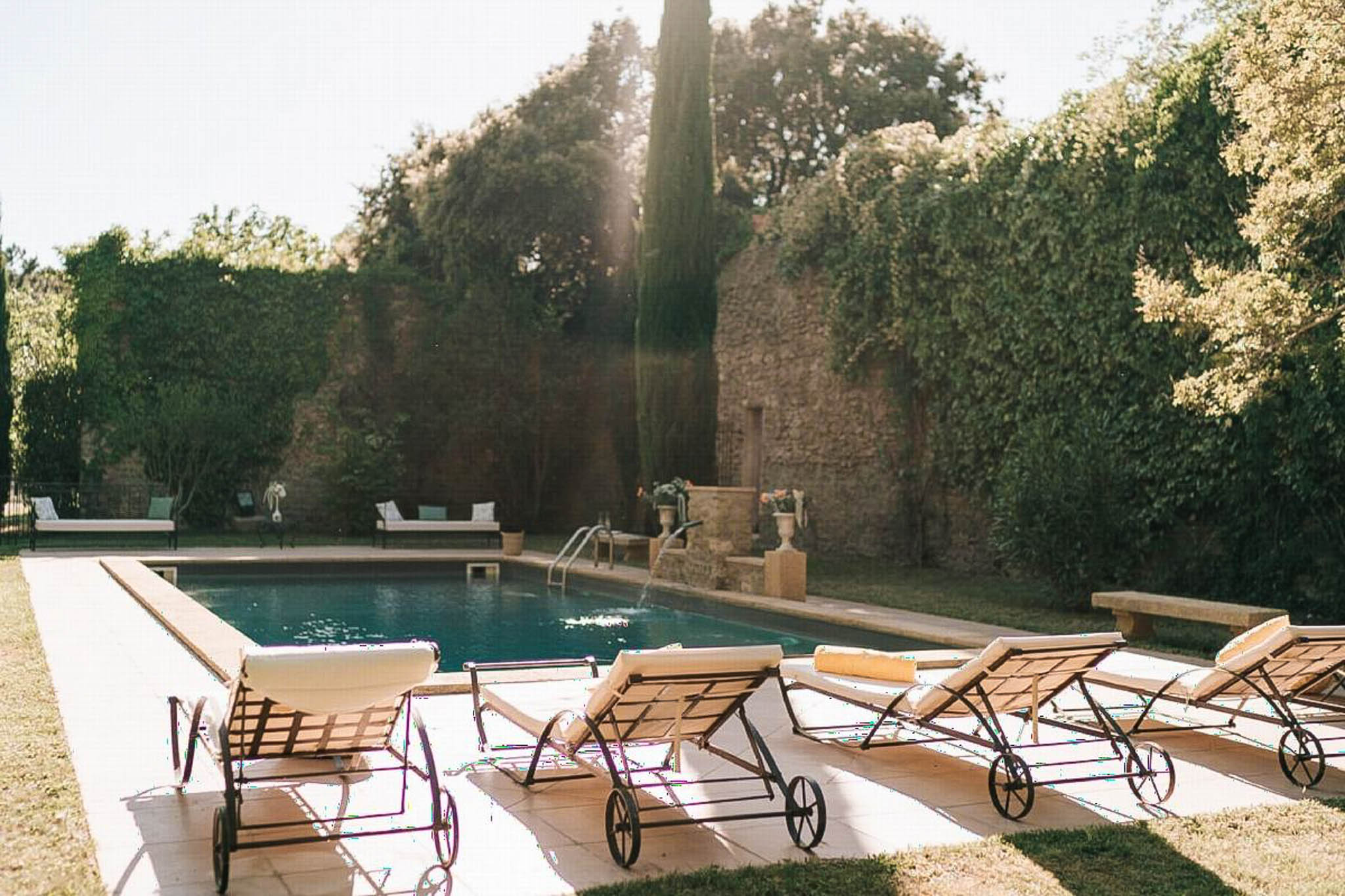 Pool terrace with sun loungers, stone urns, and hedging at a French country estate
