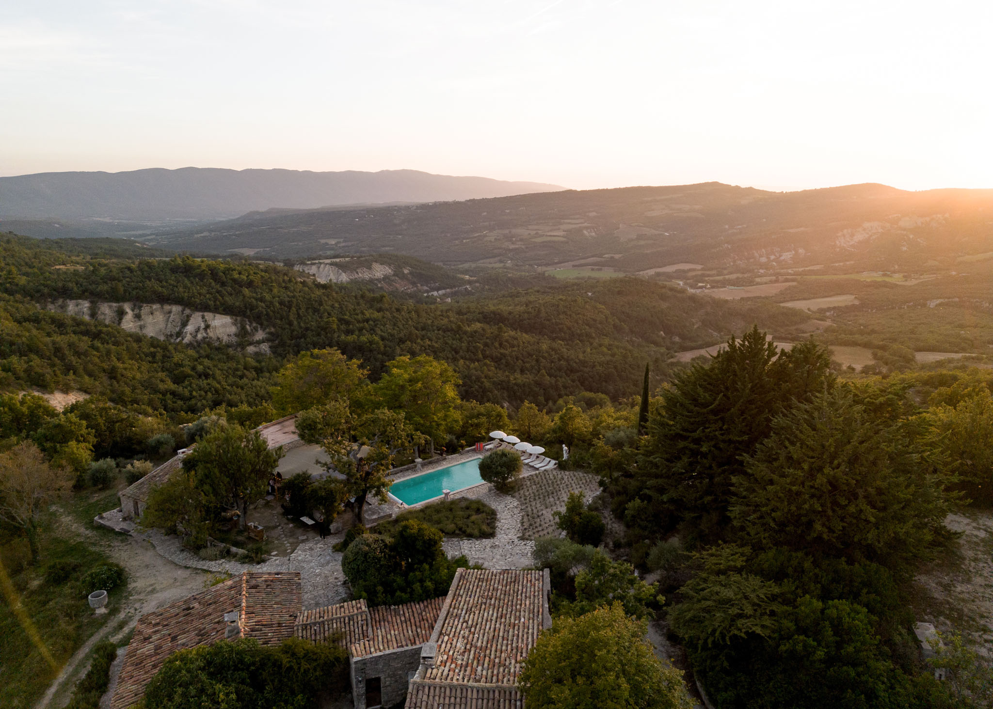 Aerial view of Provencal stone mas with turquoise pool and terrace at golden hour, valley and mountains beyond