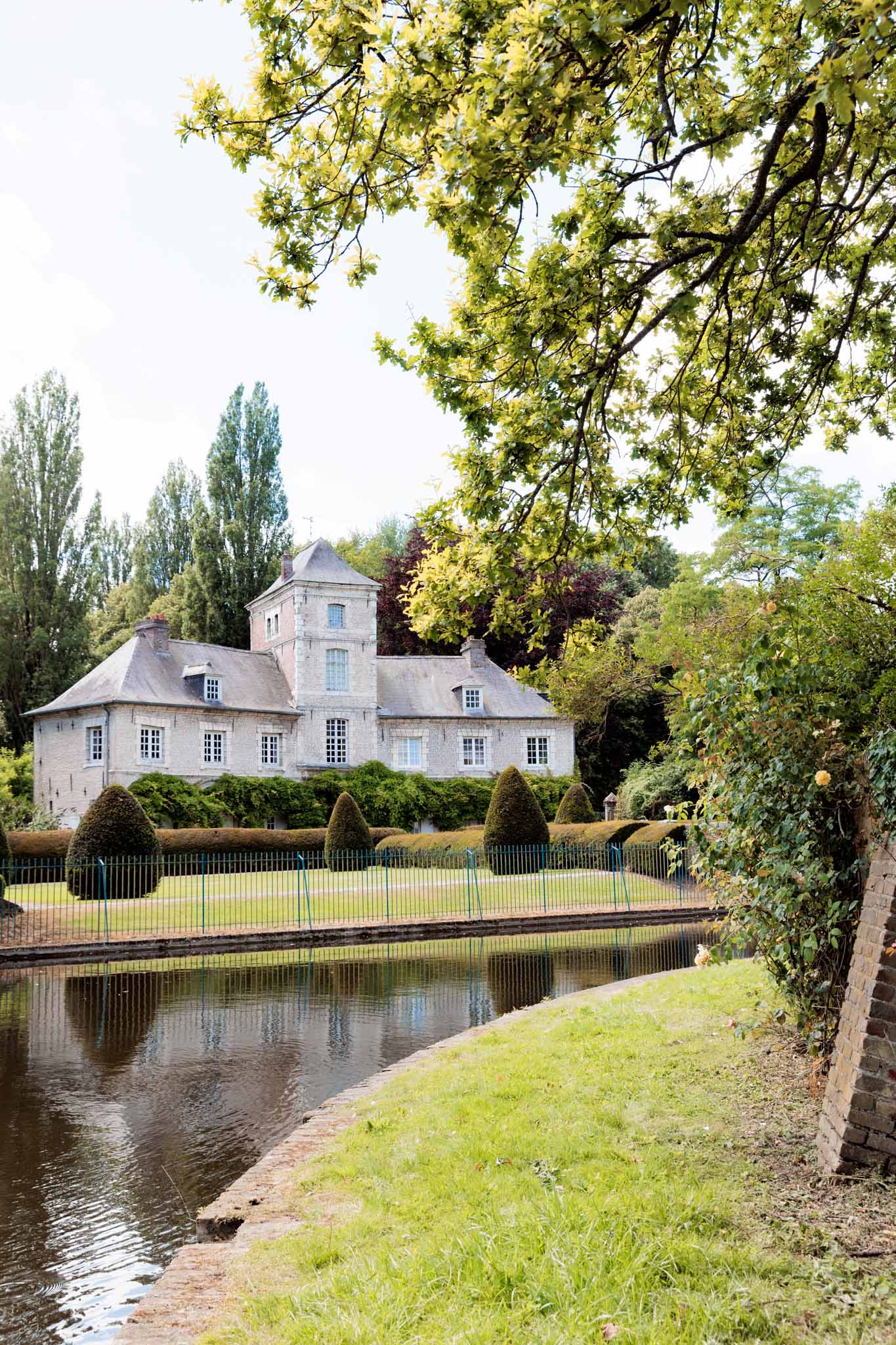 French manor house with square tower reflected in a still pond, formal topiary garden in foreground