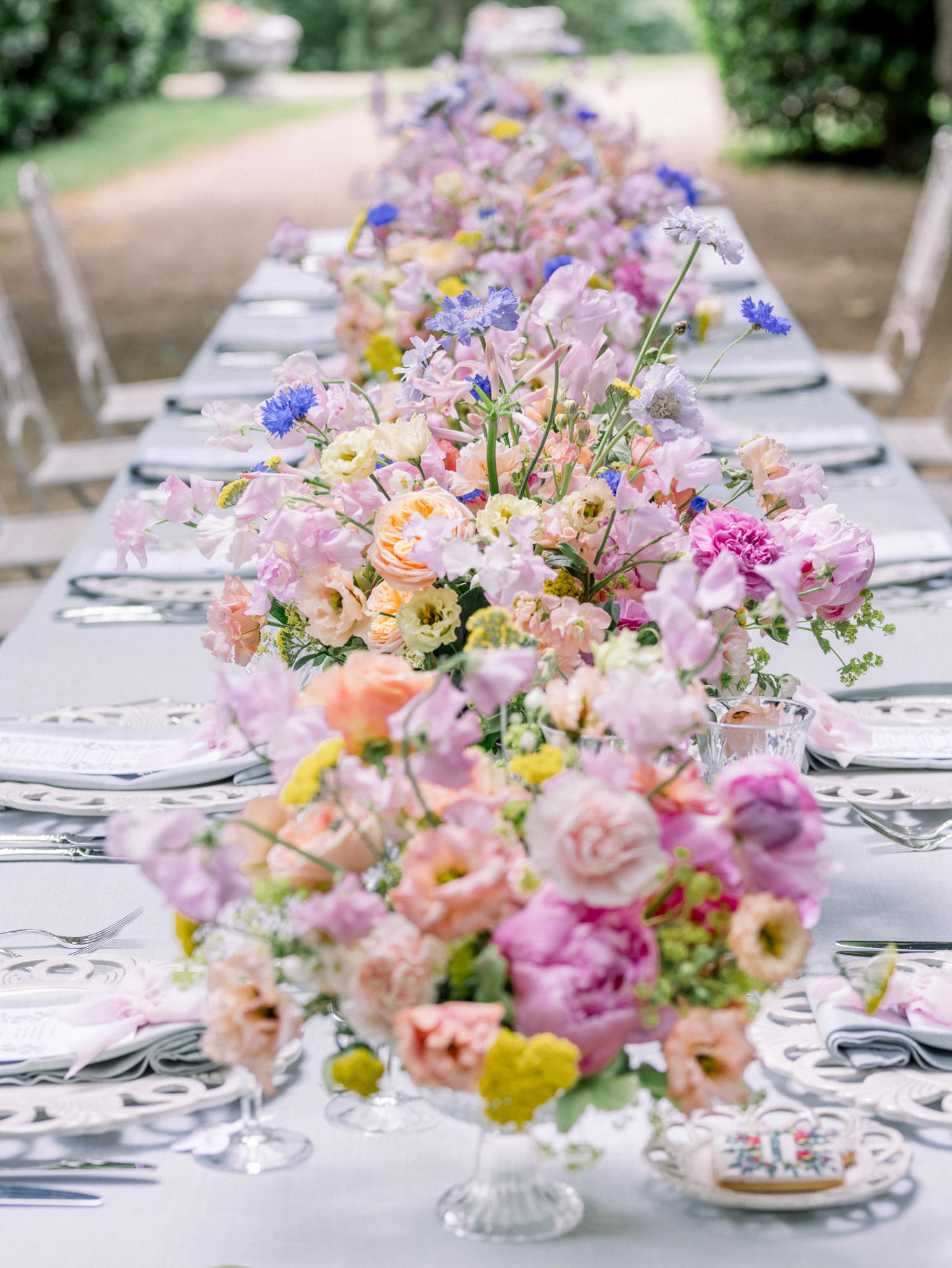 Reception table garland with pink roses, magenta peonies, blue cornflowers, and white ranunculus in glass vessels
