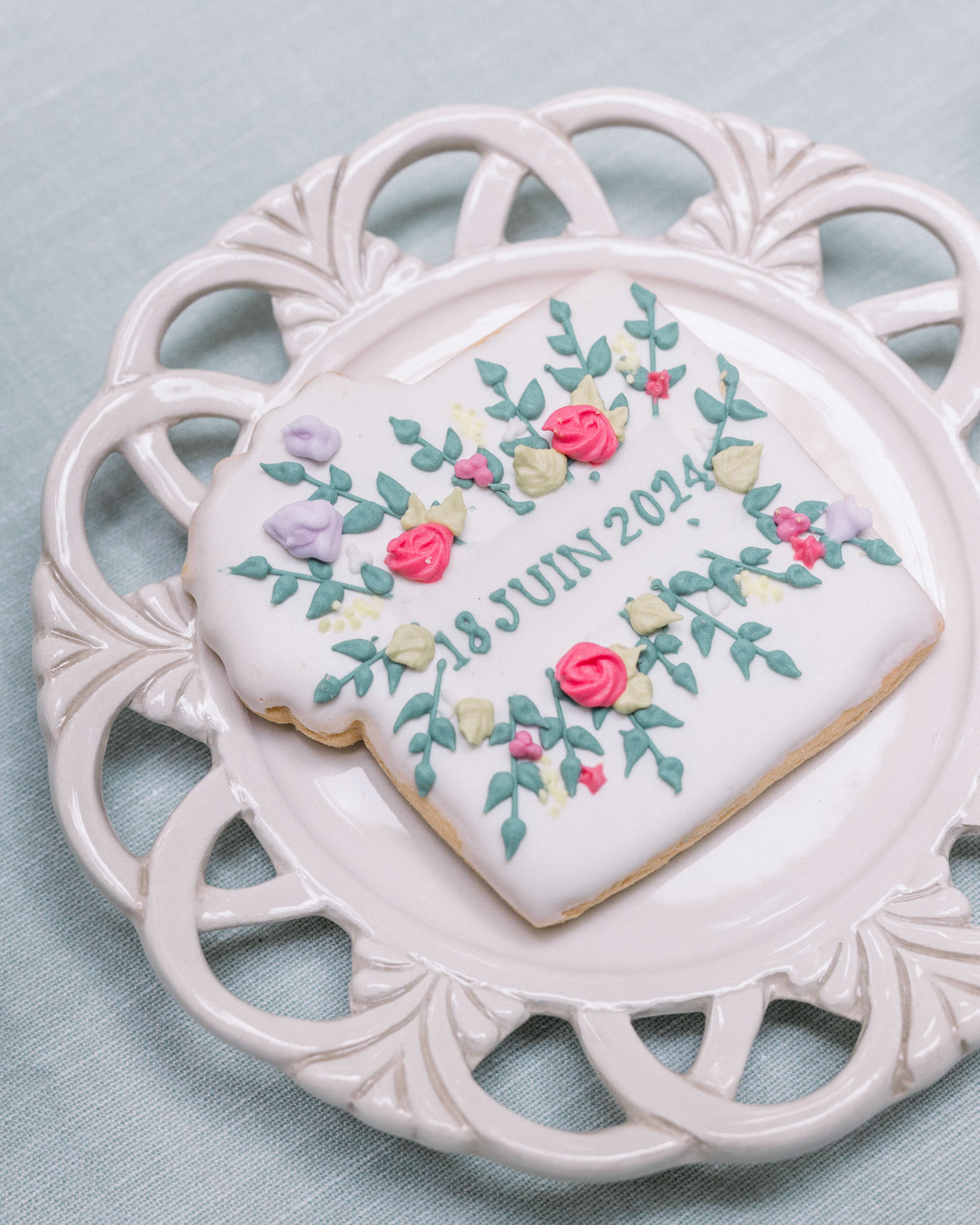 Heart-shaped wedding cookie with floral icing and date on ornate white porcelain plate
