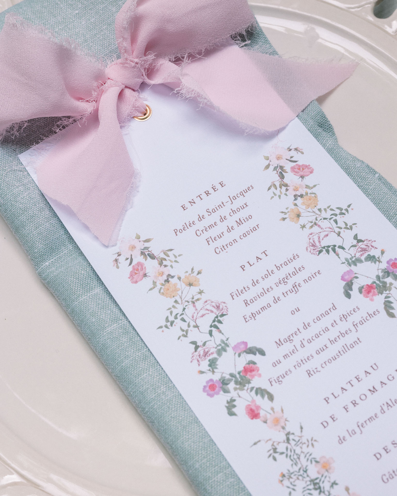 Wedding menu card with floral border tied with mauve ribbon on sage green napkin and white plate
