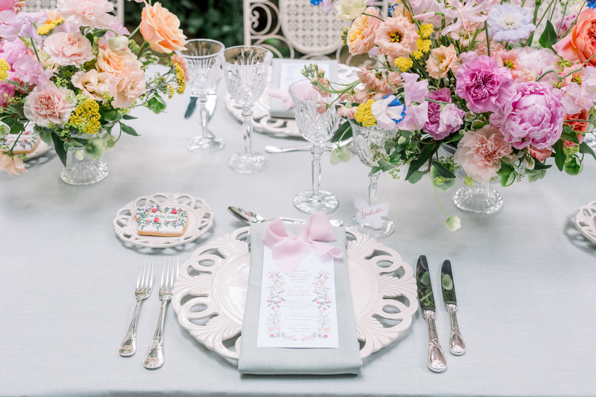Reception place setting with ornate white charger, pink bow napkin, and peonies and garden rose centerpieces