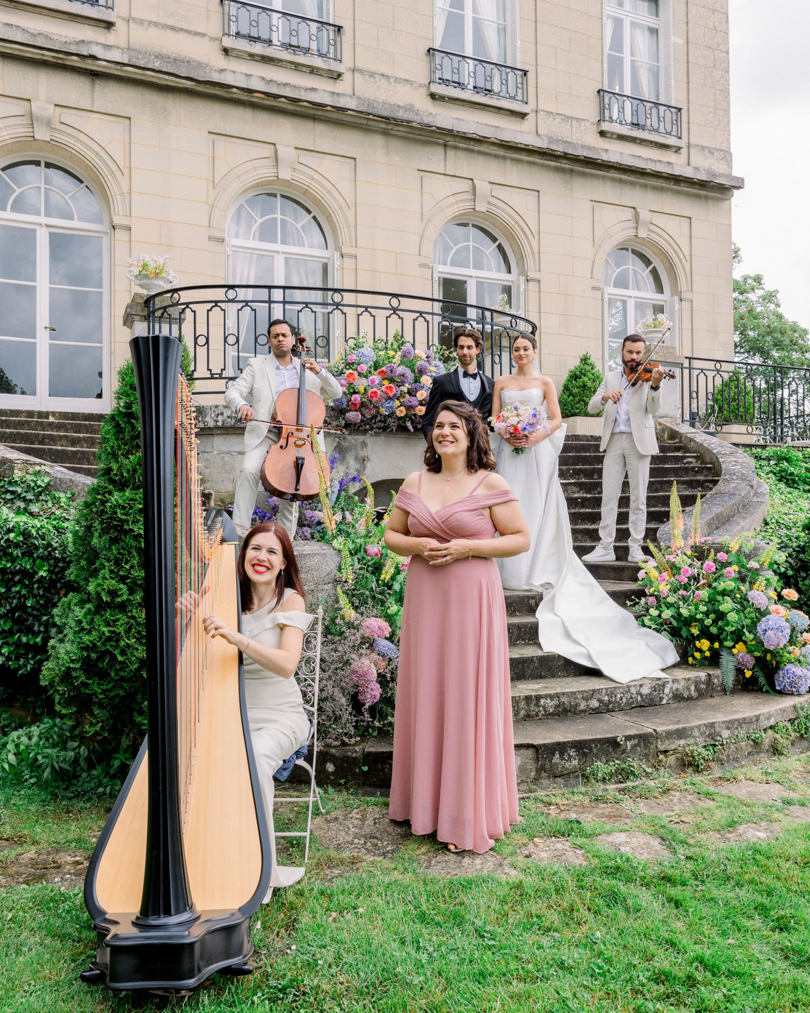 Group portrait on stone steps of classical mansion with bride holding colourful bouquet