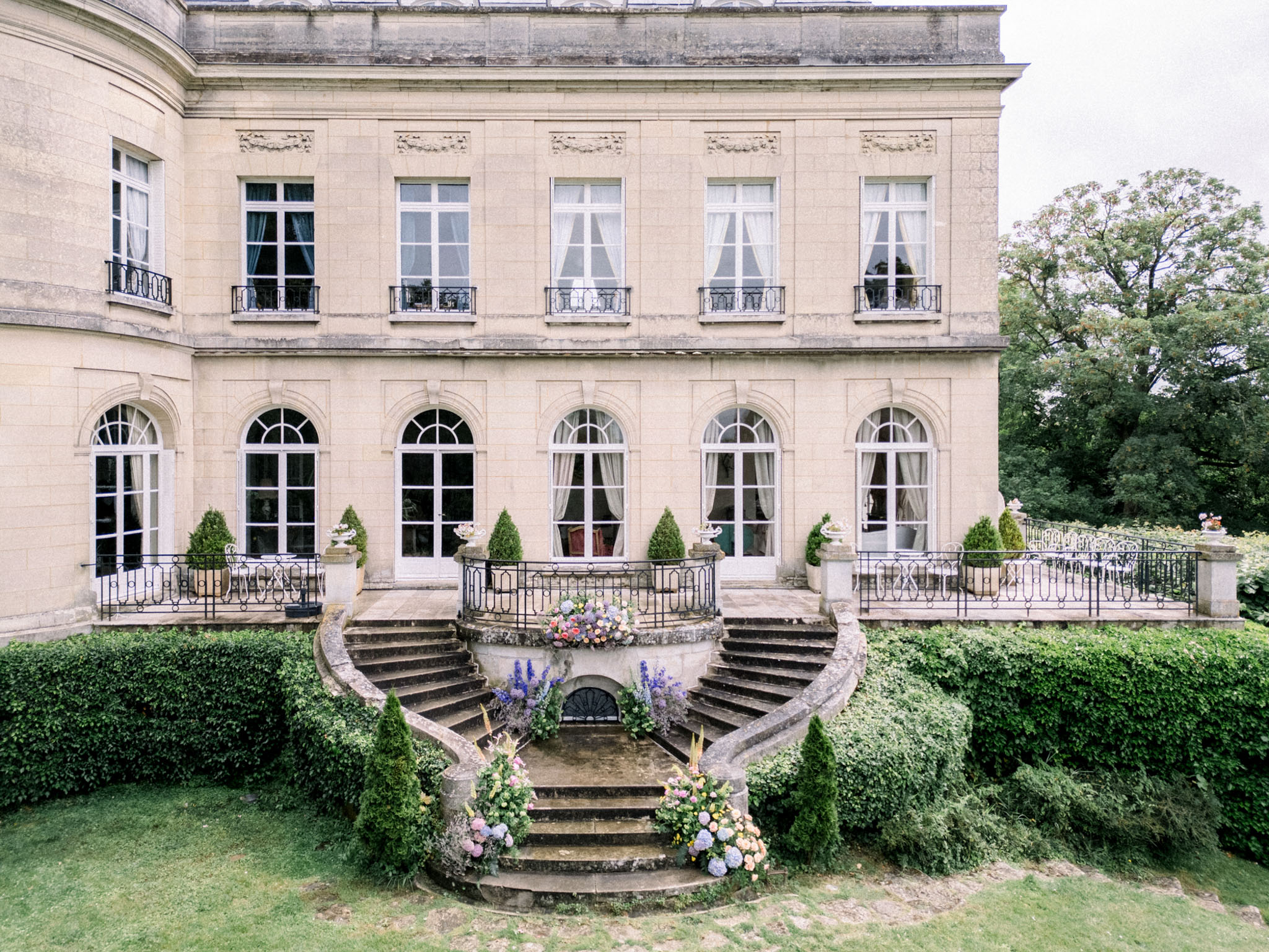 Classical French stone mansion facade with arched windows, curved staircase and pink and lavender floral arrangements