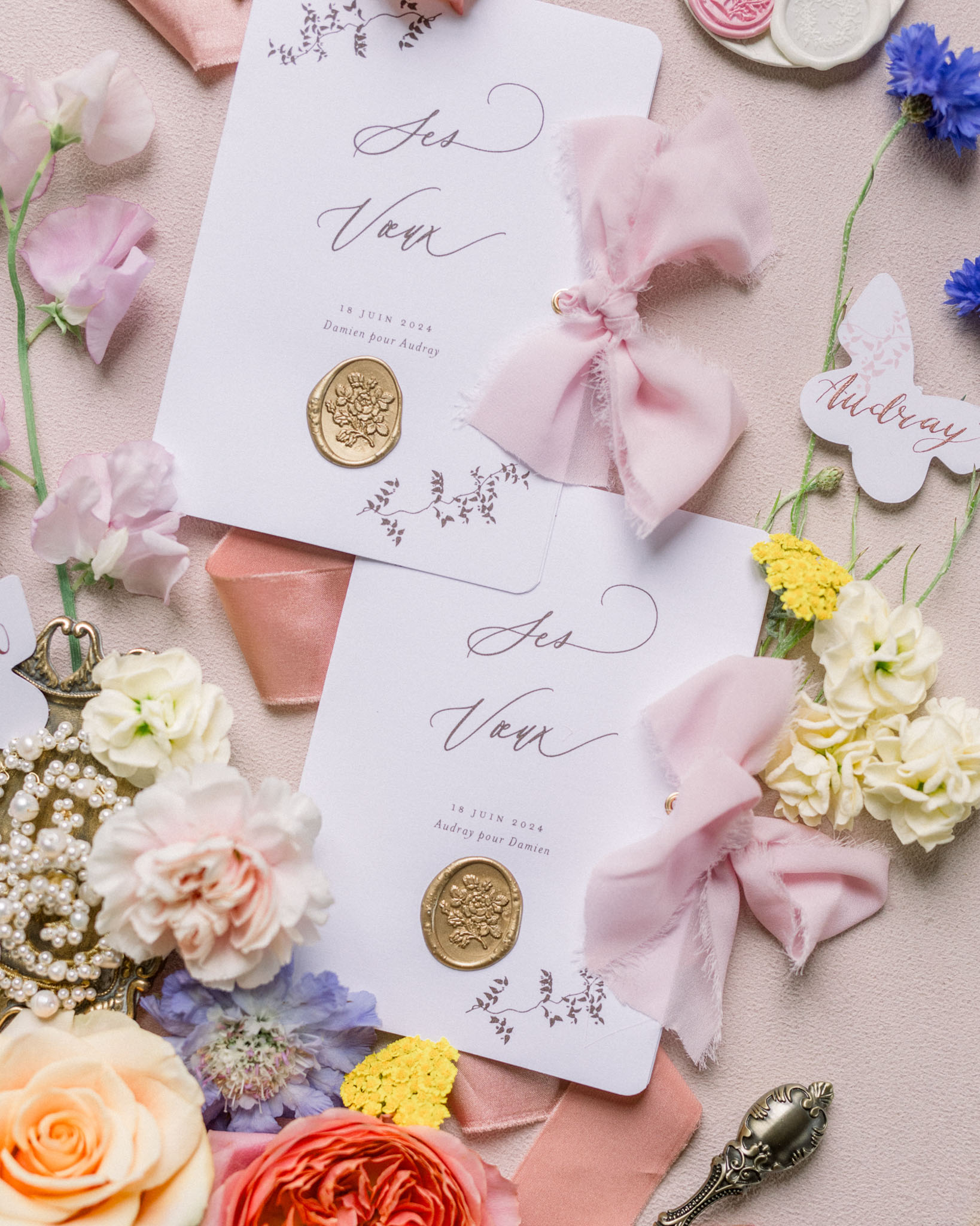 Wedding stationery flat lay with ivory invitations, gold wax seals, dusty pink ribbons, and scattered garden florals