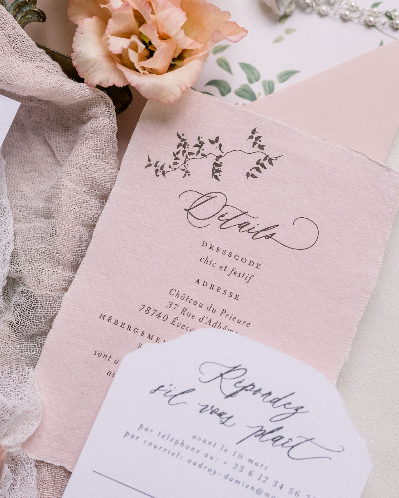 Flat lay of pink wedding invitation with calligraphy alongside fresh flowers and ribbon
