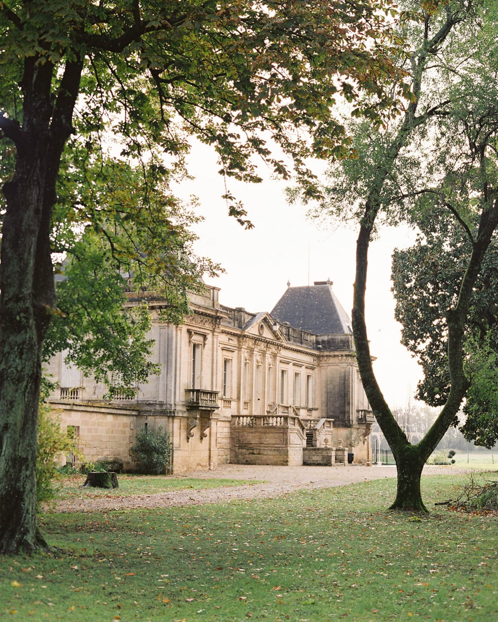 Classical limestone chateau with mansard roof stone balustrades and autumn lawn framed by trees