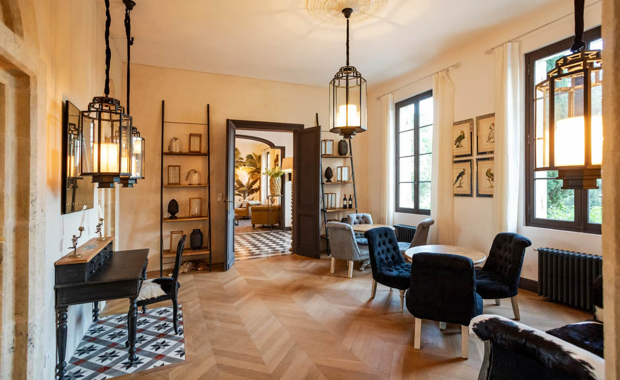 Interior of chateau reception room with herringbone floors, navy armchairs, lantern pendants, and eclectic decor
