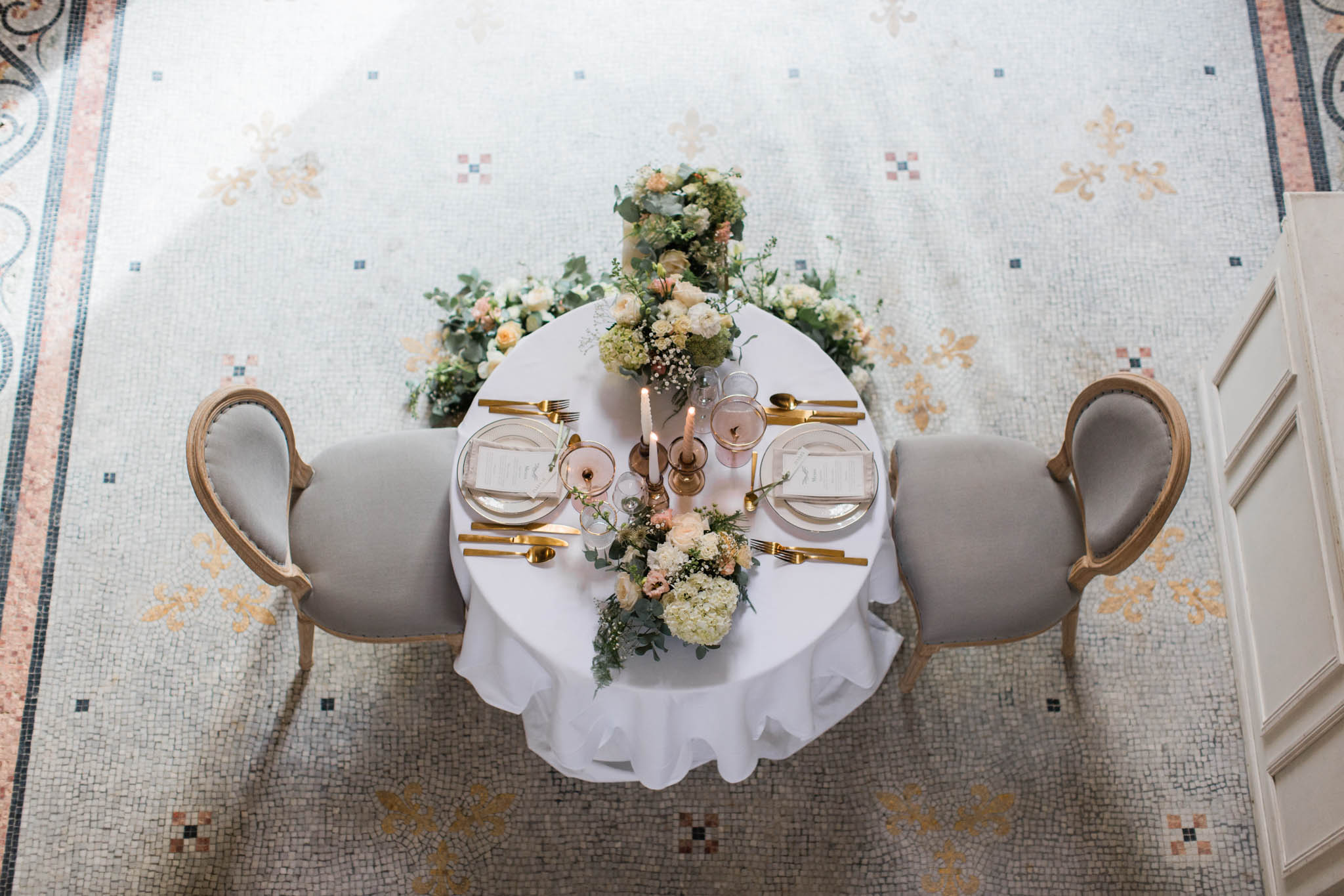Overhead view of intimate round reception table with cream and peach rose centerpiece on geometric mosaic tile floor