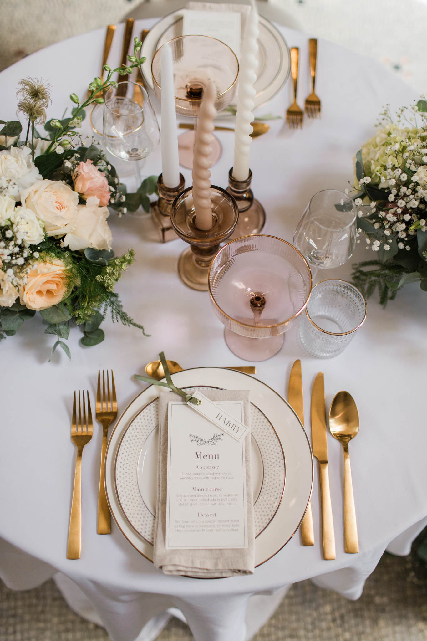 Overhead flat lay of reception table with rose-gold rimmed plates, gold flatware, cream taper candles, blush centerpiece